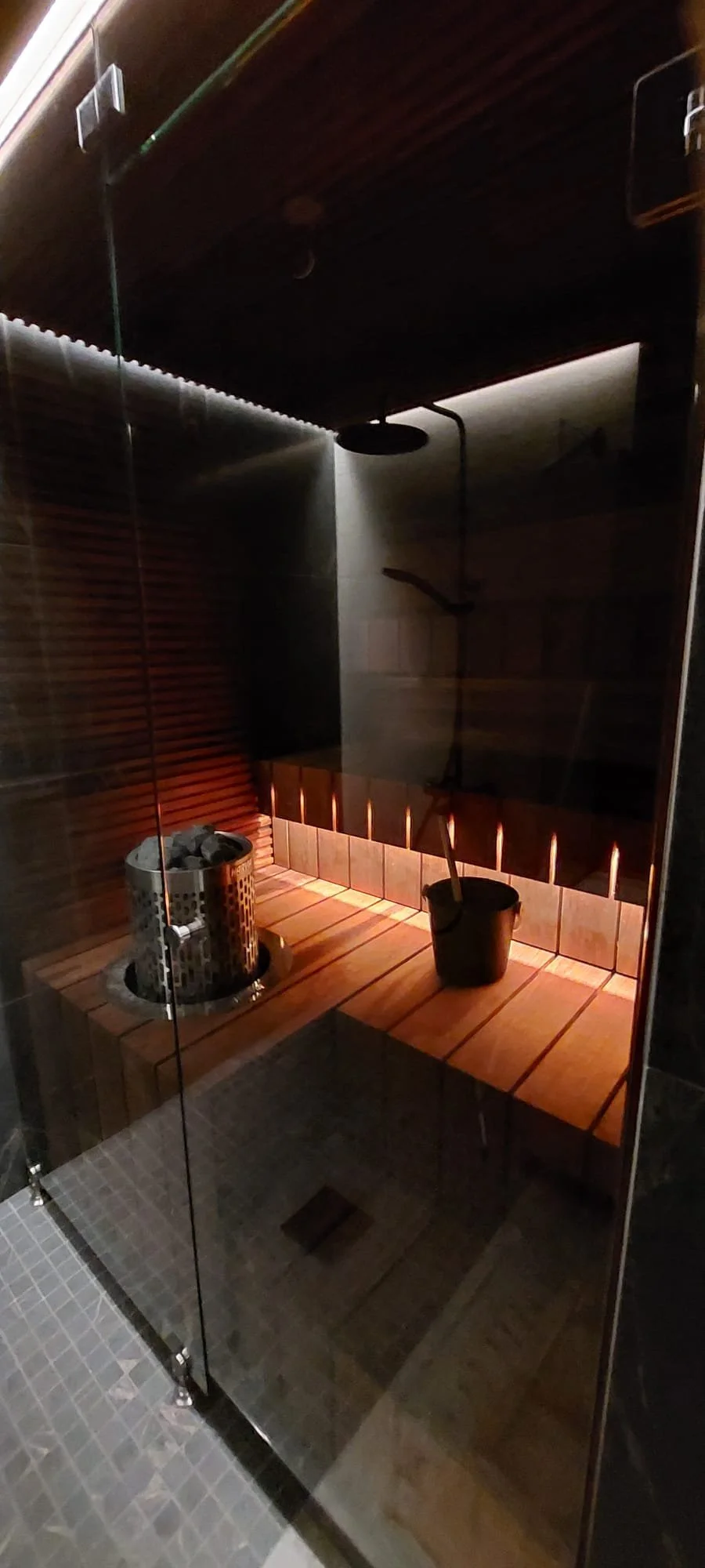 Lämmitetty sauna, jossa on kiviä ja kiulu, iltavalaistus ja lasiseinät.
