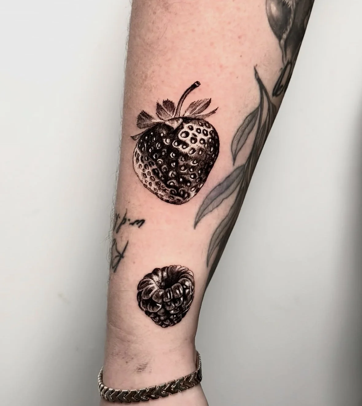 Tattoo of a strawberry with leaves and a raspberry above a word or phrase on the person's forearm. Small realistic tattoo by Rose F tattoo in Bristol UK, soon to be Sunshine Coast in Queensland near Brisbane, Australia 