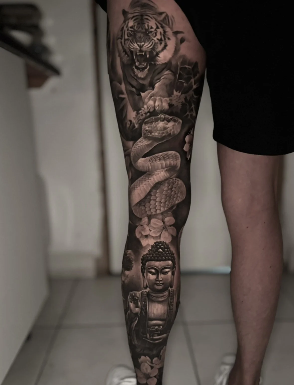 Tattoo sleeve featuring a tiger in a roar, a snake coiled around flowers, and a Buddha figure on the lower leg. detailed black and grey work by Rose F Tattoo in Bristol, UK, soon to be in Sunshine Coast, near Brisbane, QLD, Australia