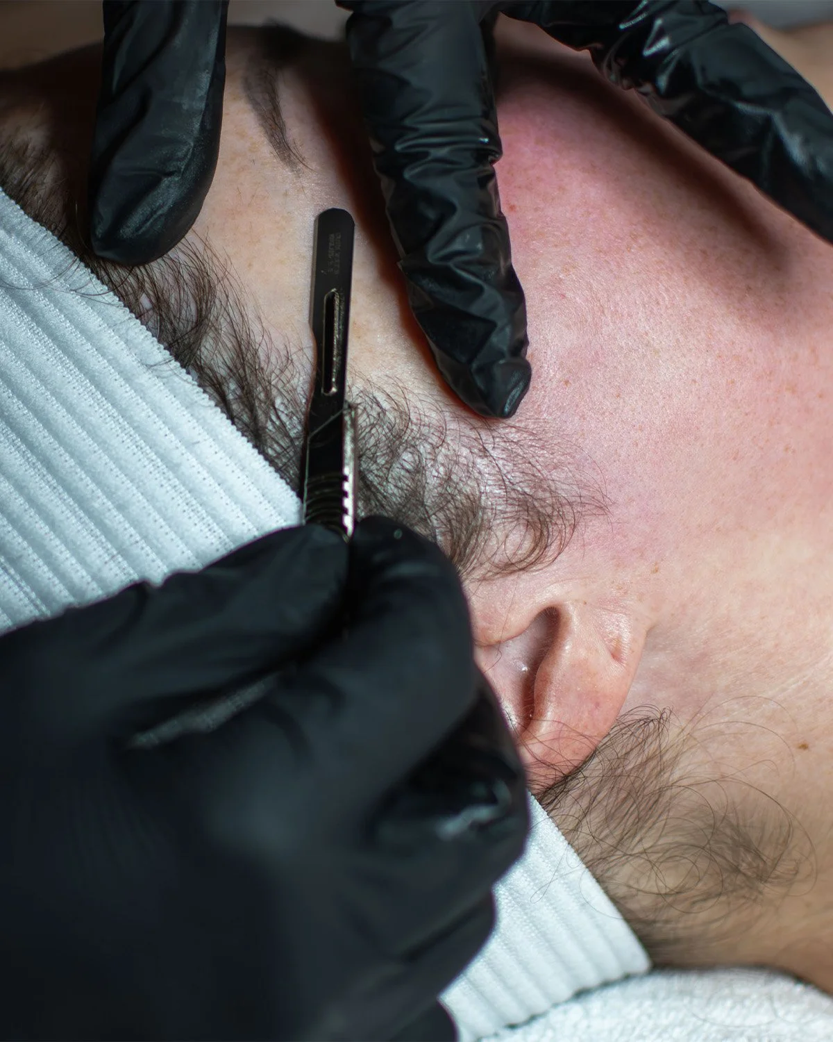 Person wearing black gloves getting an ear piercing with a tattoo needle.