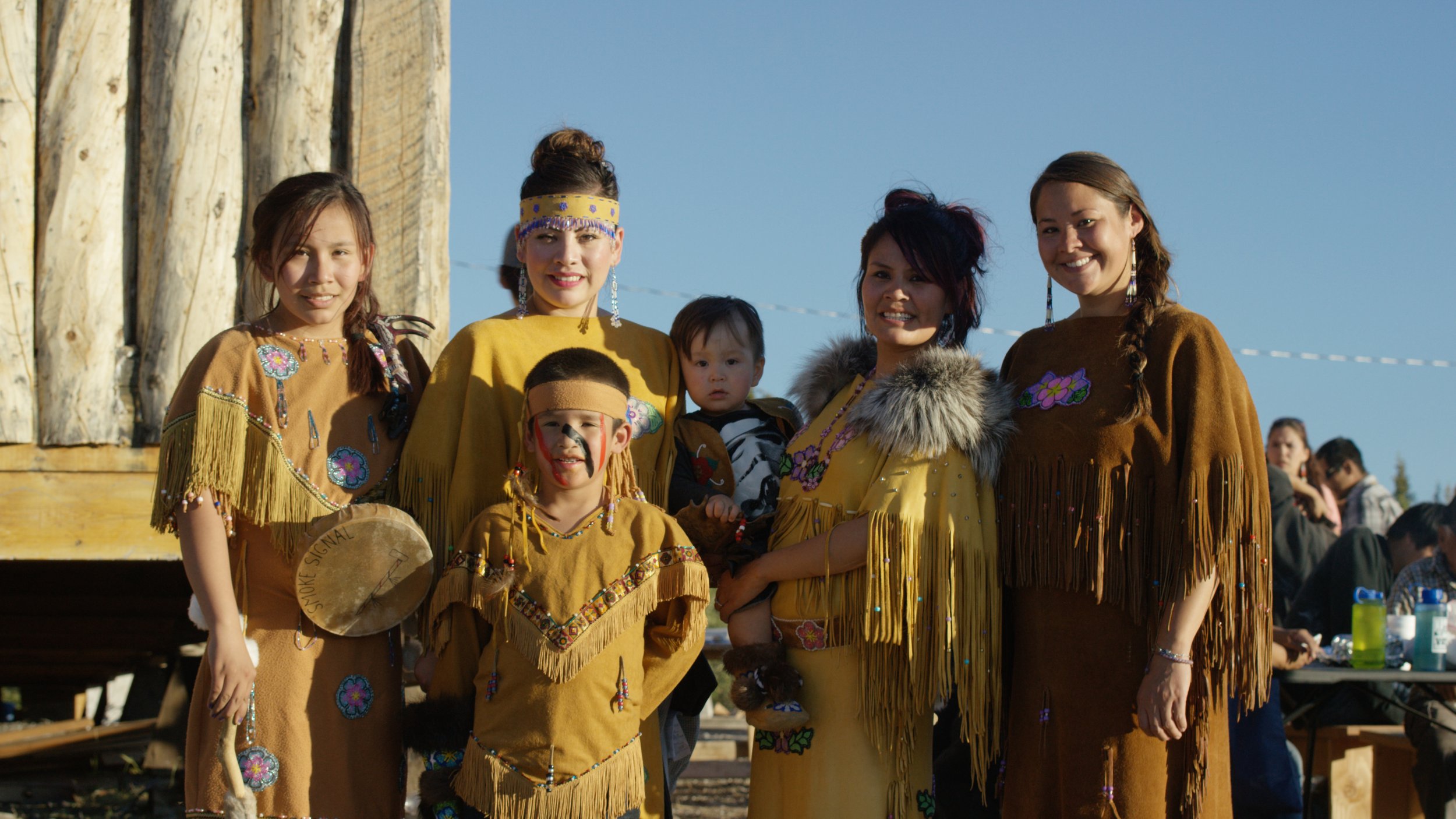 Group of women and children in traditional Native American clothing, posing outdoors.
