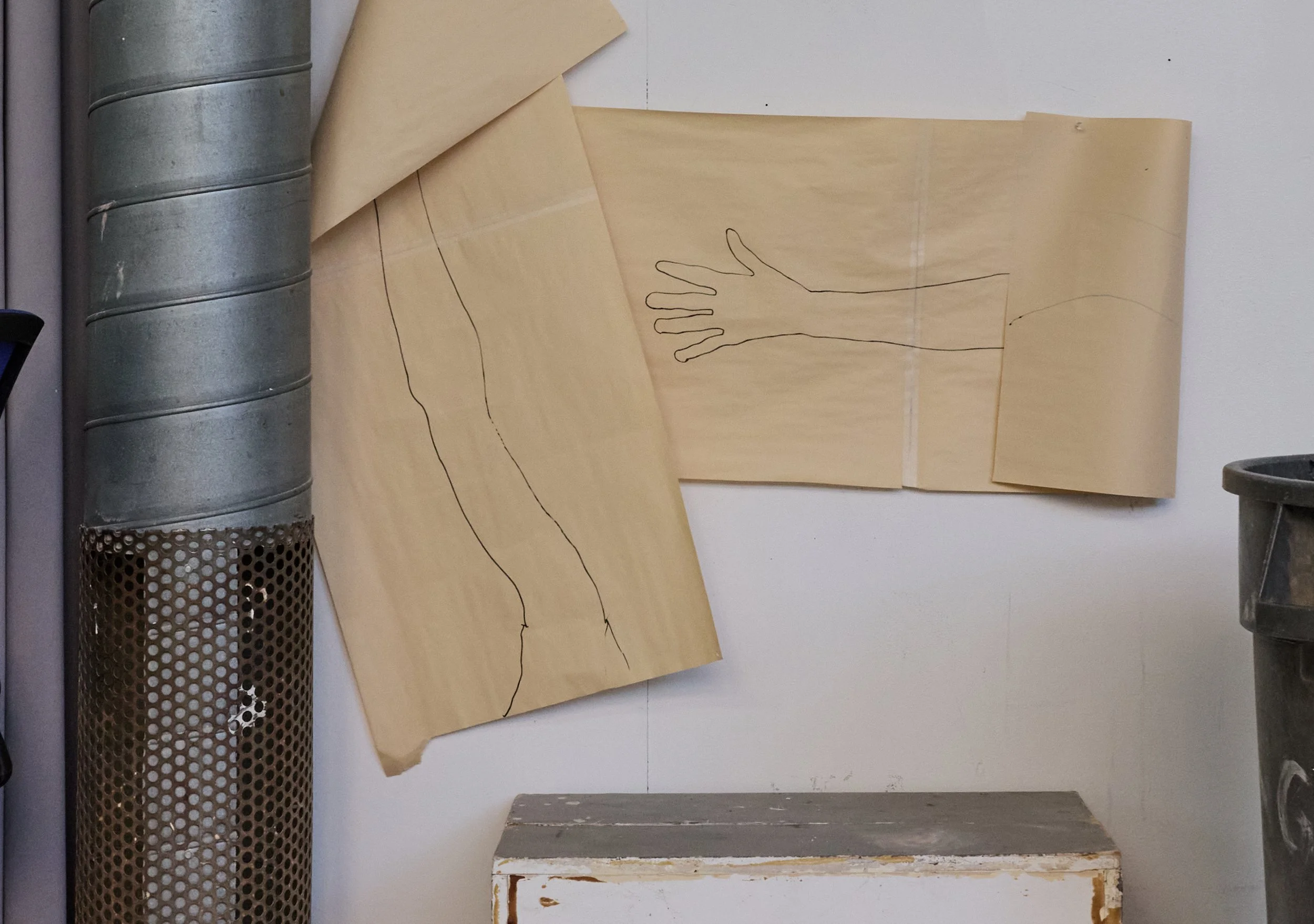 Tan poster paper with life size drawings of human arms, barely holding on to the wall with tape, showing unfinished work left behind in VIA.