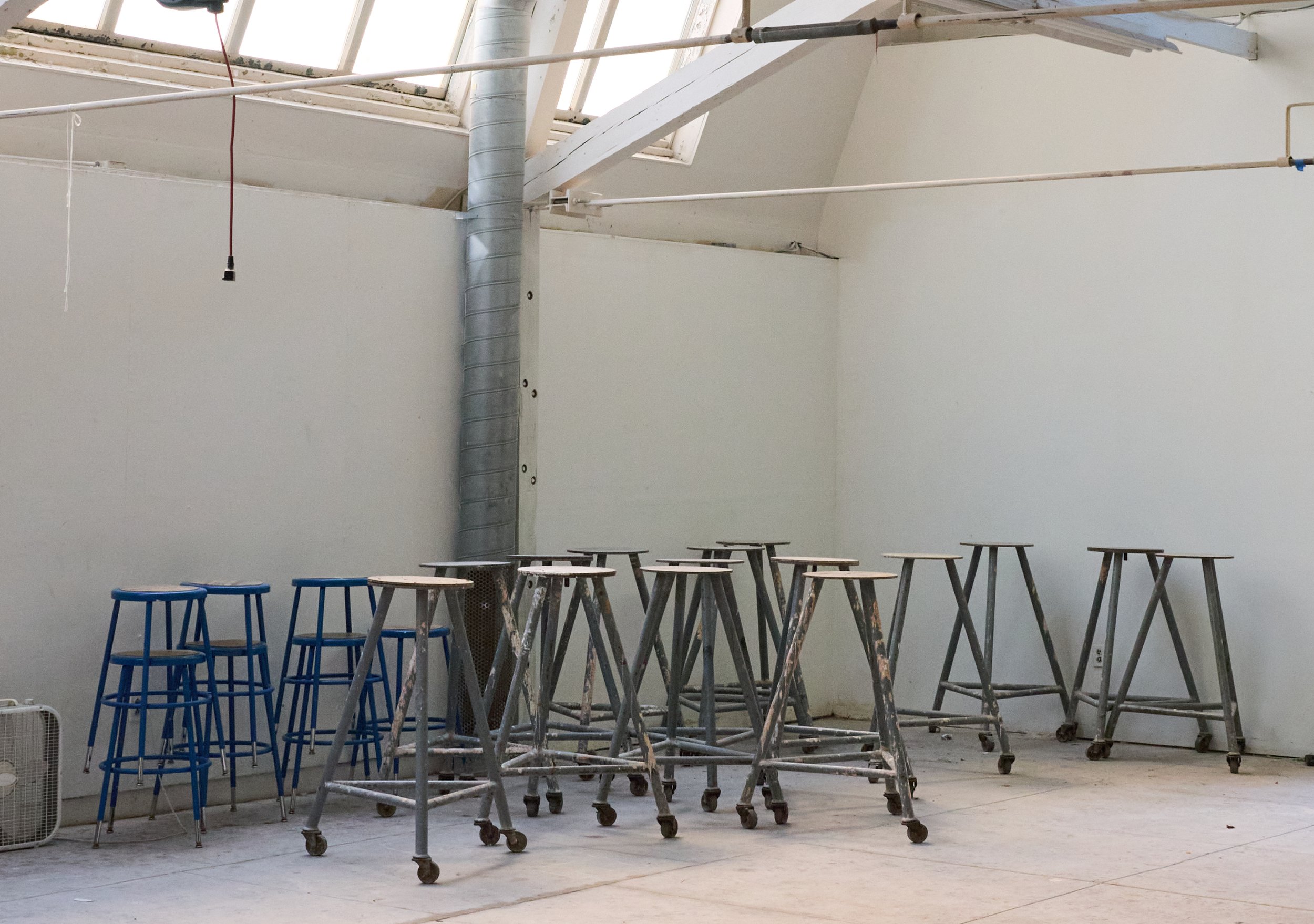 A skylight-lit studio space with a collection of stacked stools and mobile pedestals, showing potential for former classrooms to continue being used for the arts.