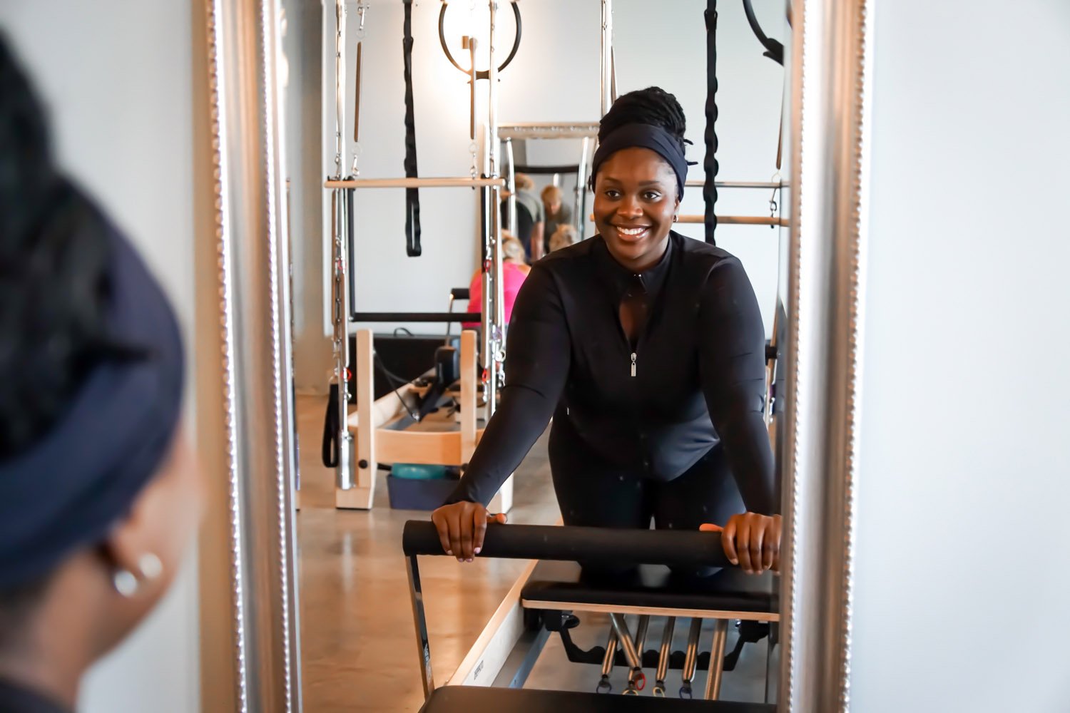 A woman smiling at herself in a mirror while exercising on a reformer machine at Body & Soul Pilates in Gluckstadt, MS