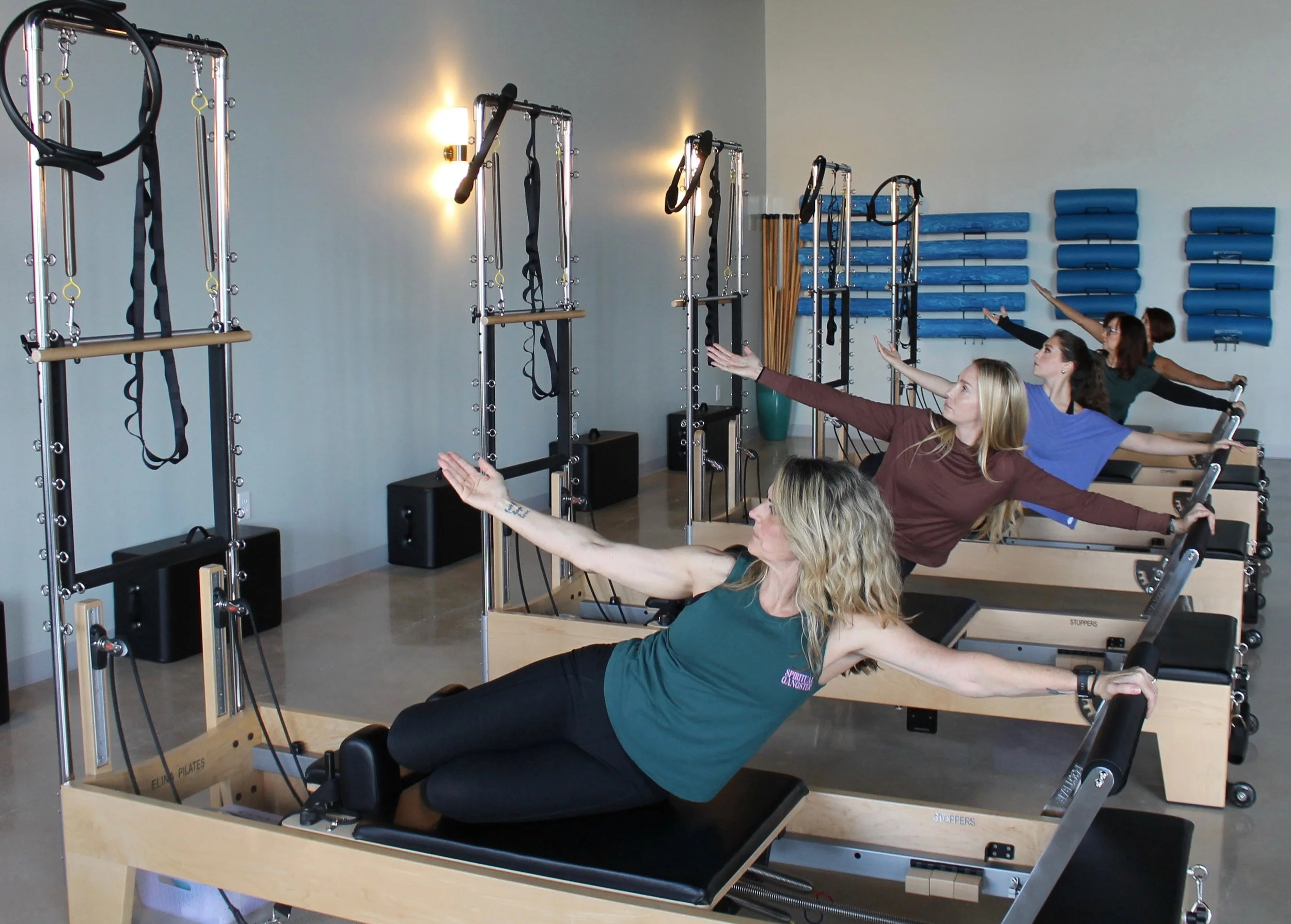 Four women participating in a Pilates class using reformer machines at Body & Soul Pilates in Gluckstadt, MS, performing an exercise with their arms extended.