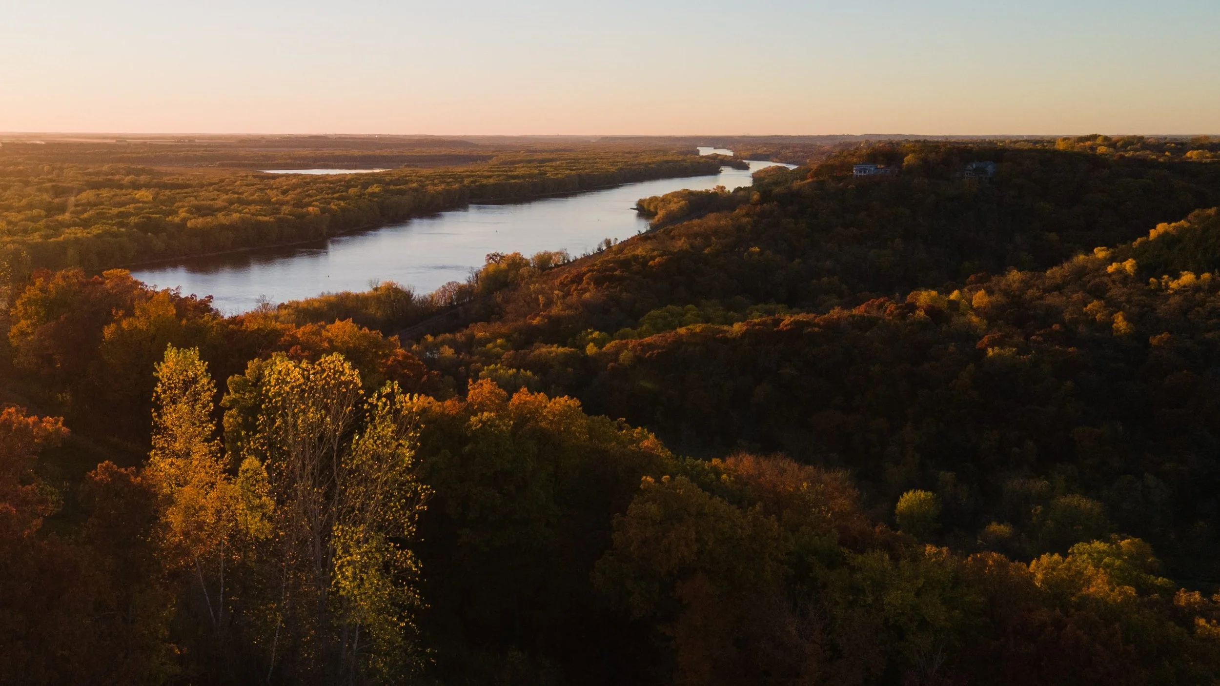 A scenic aerial view of a winding river flowing through a forested landscape during autumn, with colorful fall foliage and a clear sky.