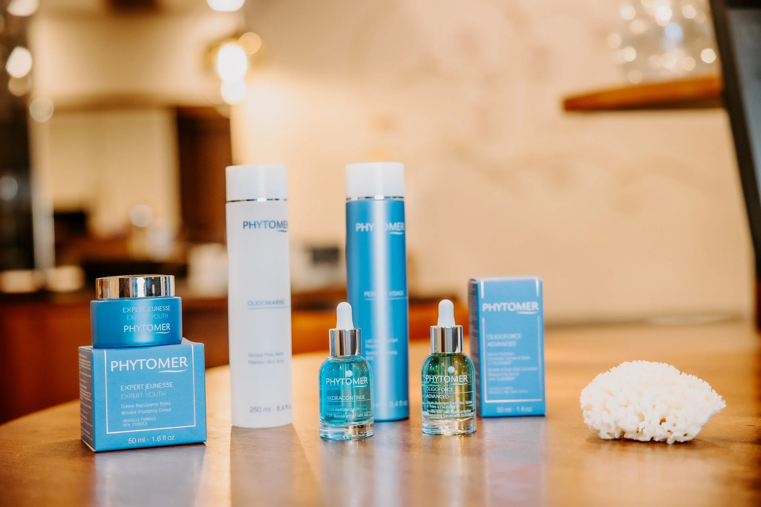 Pflegeprodukte, darunter Cremes und Seren, auf einem Holztisch, mit einem weißen Schwamm am rechten Rand.