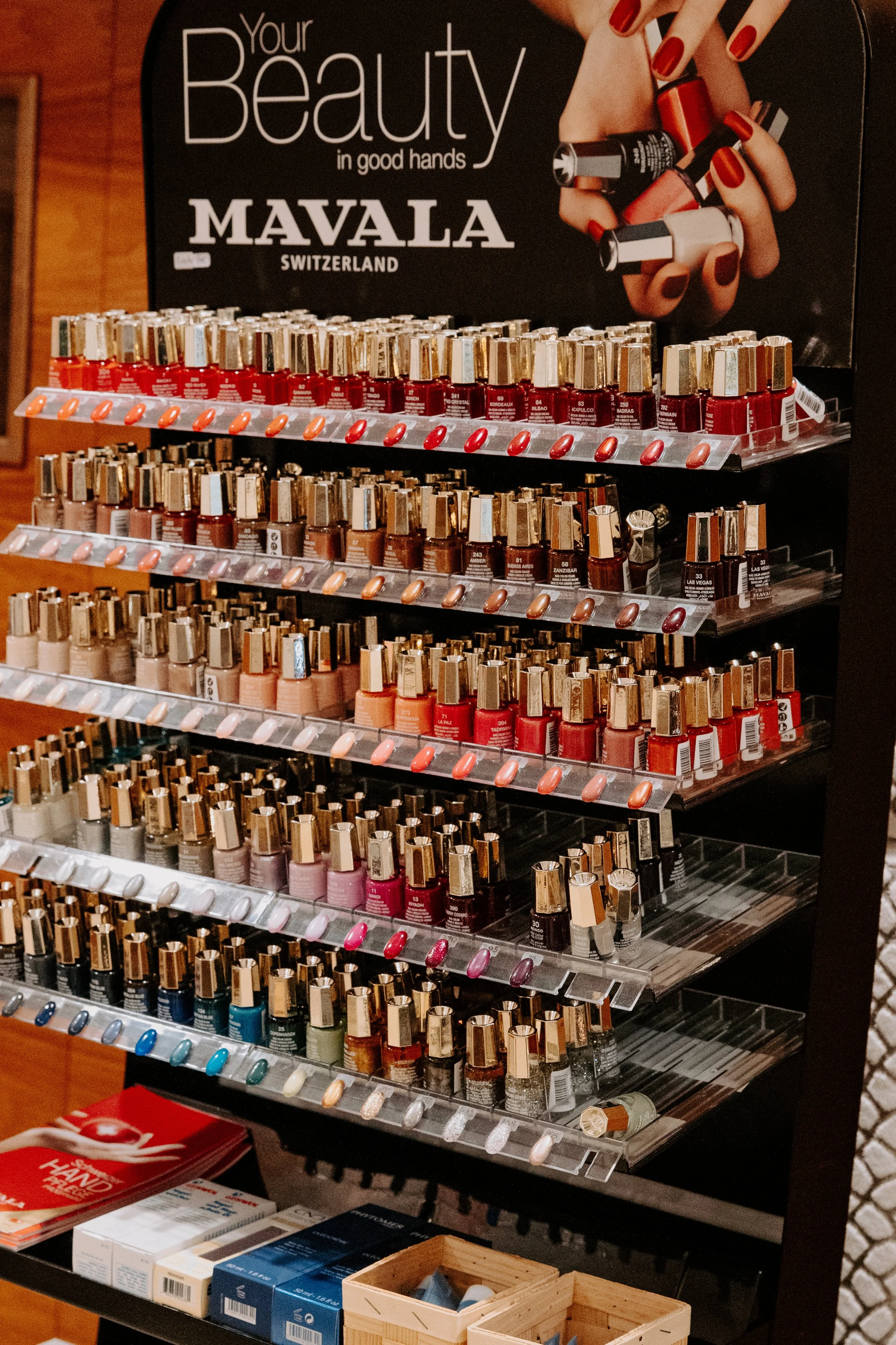 Verschiedene Nagellackflaschen auf einem Regal, oben ein Schild mit dem Text "Your Beauty in good hands" und "MAVALA Switzerland".