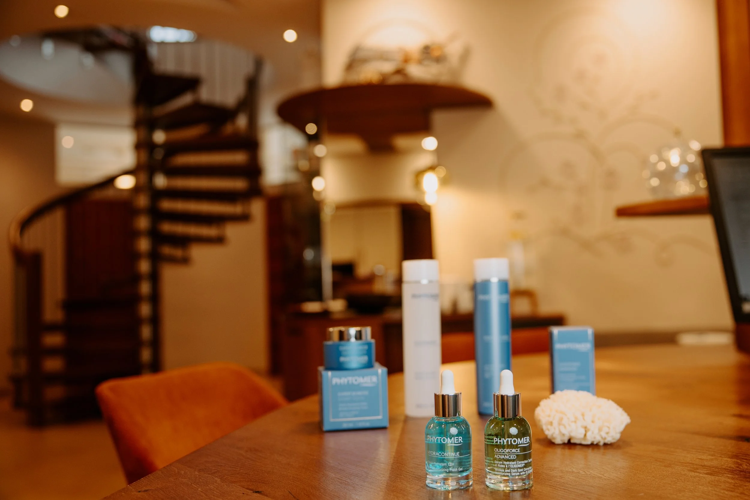Hautpflegeprodukte auf einem Holztisch in einem warm beleuchteten Raum, im Hintergrund eine moderne Treppe.