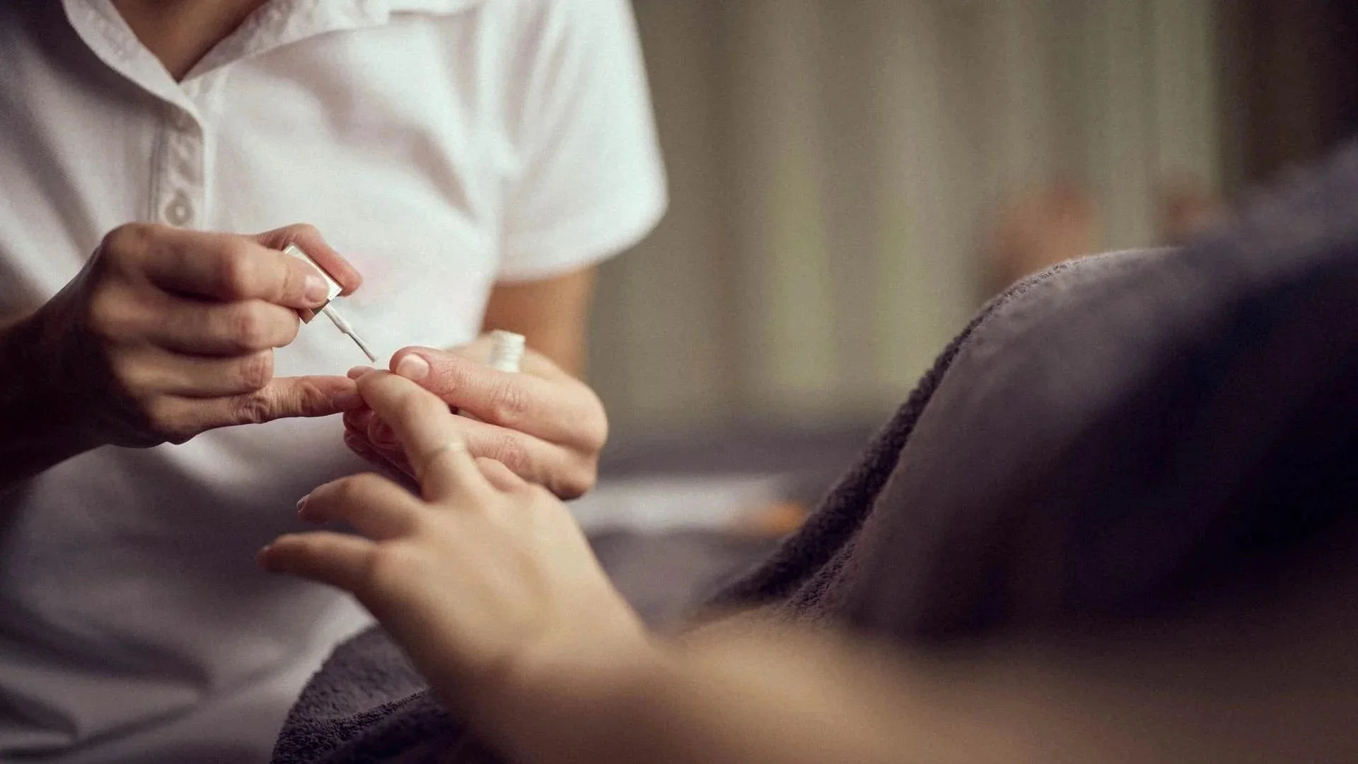 Eine Person erhält eine Maniküre, während eine andere Person die Nägel lackiert.