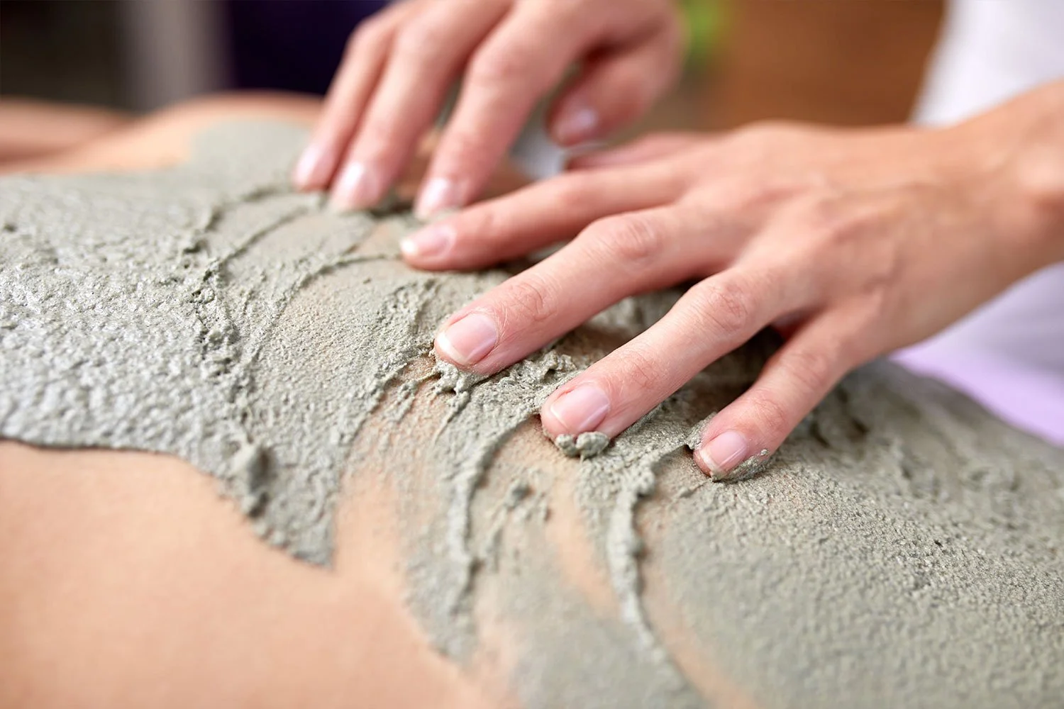 Person beim Auftragen von feuchtem Sand auf Haut, vermutlich bei einer Massage oder Schönheitsbehandlung.