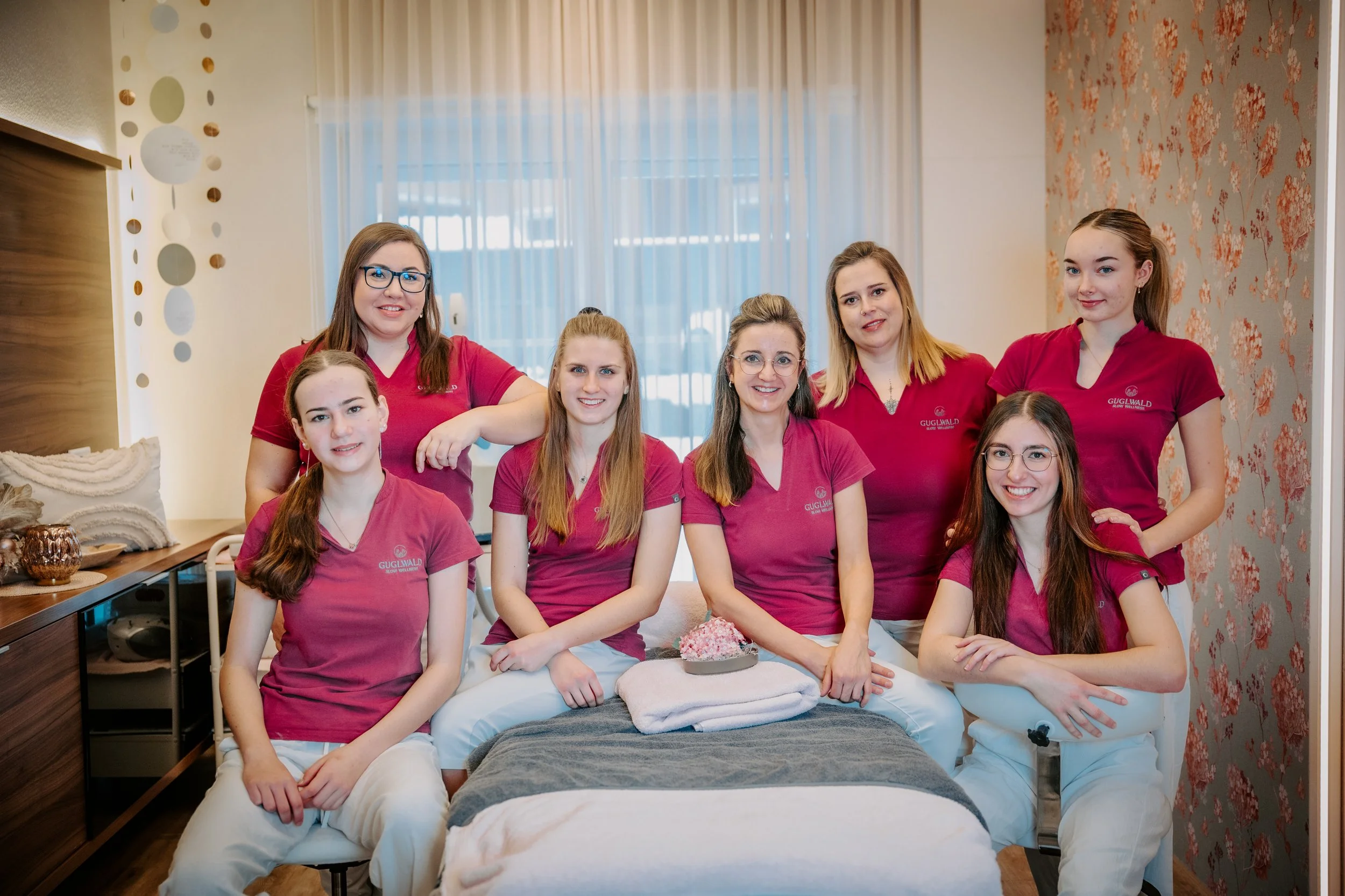 Sieben Frauen in roter Arbeitskleidung in einem Spa- oder Wellnessraum.
