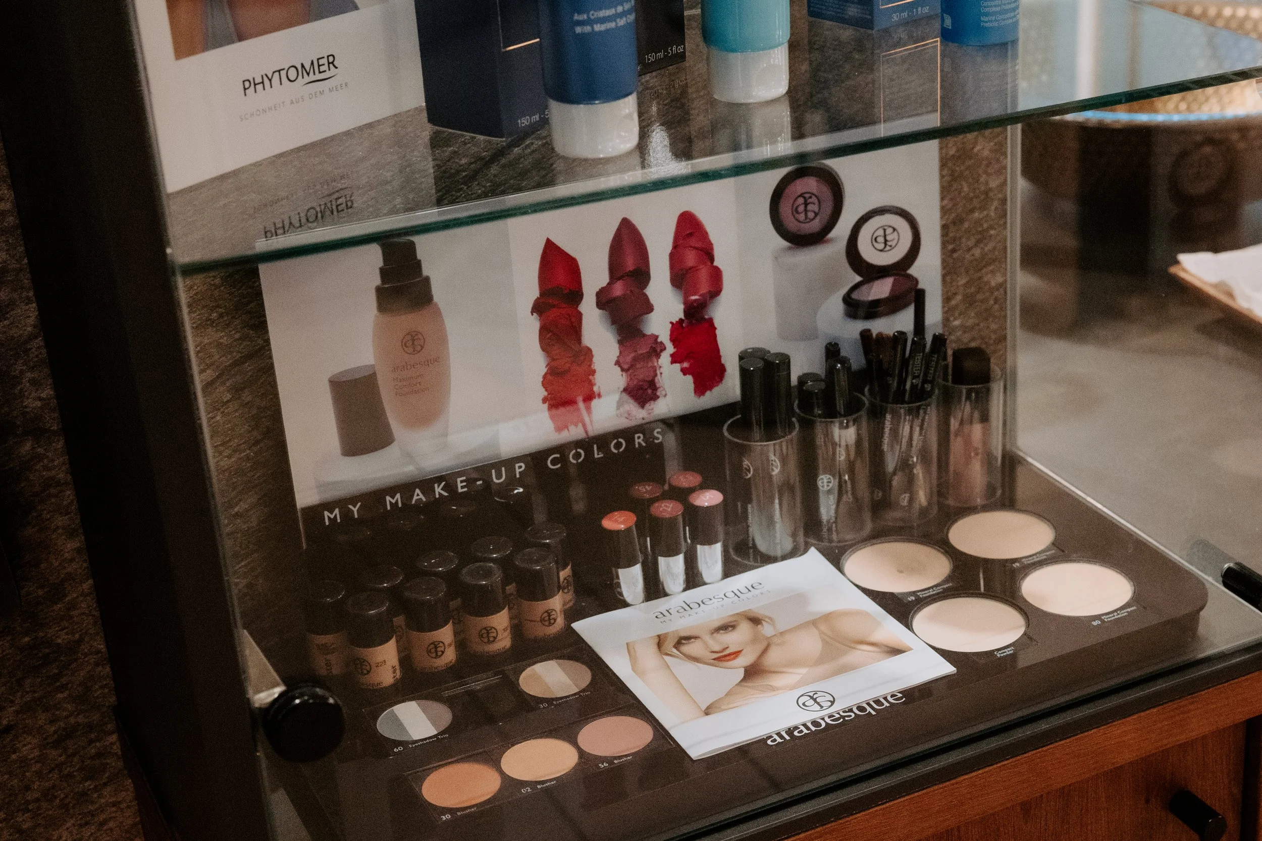 Verkaufsdisplay mit verschiedenen Make-up-Produkten, inklusive Lippenstiften, Puder, und Kosmetikproben, mit Markenlogos und Fotos auf den Verpackungen.