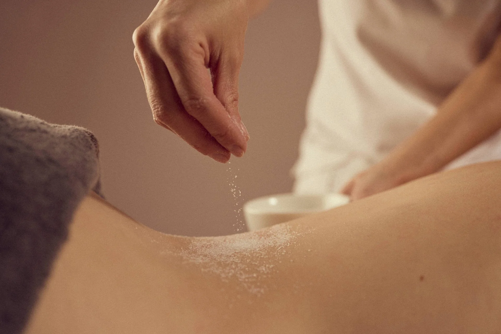 Nahaufnahme einer Person, die Salz auf den Rücken einer anderen Person streut, möglicherweise bei einer Massage.
