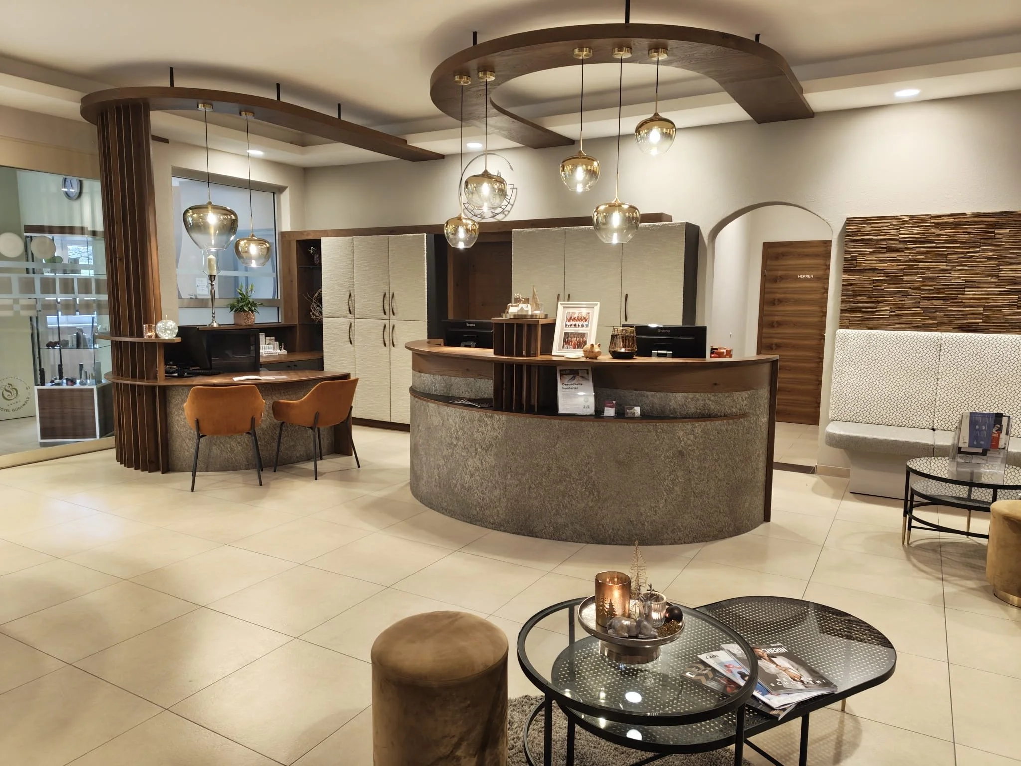 Ein modernes Lobby mit Rezeption, Sessel, einem Tisch mit Dekorationen, und einem Wartebereich mit einer weißen, gepolsterten Sitzbank.