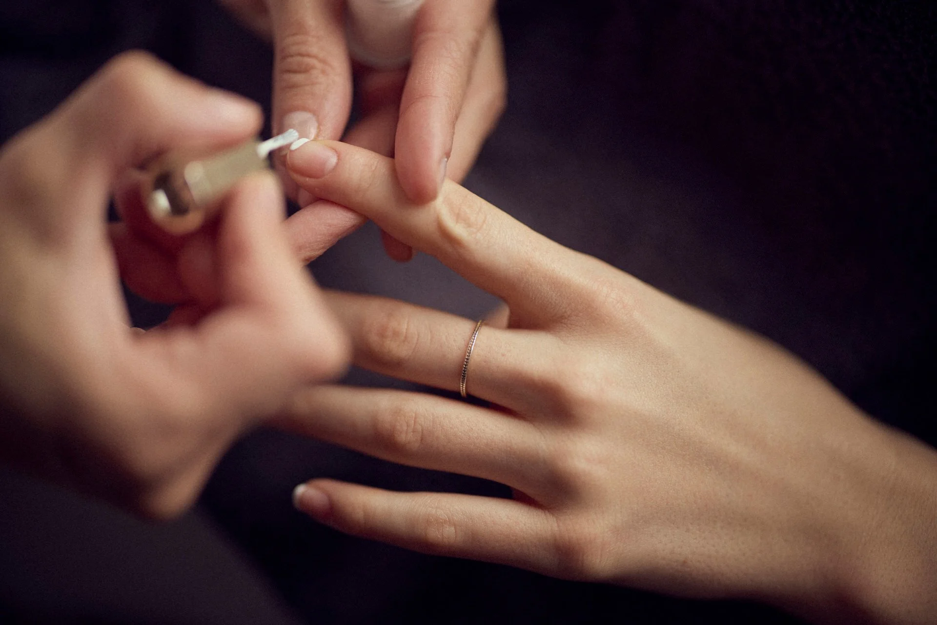 Nahaufnahme eines Menschen, der einem anderen den Fingernagel lackiert, beide Hände sichtbar, eine trägt einen goldenen Ring