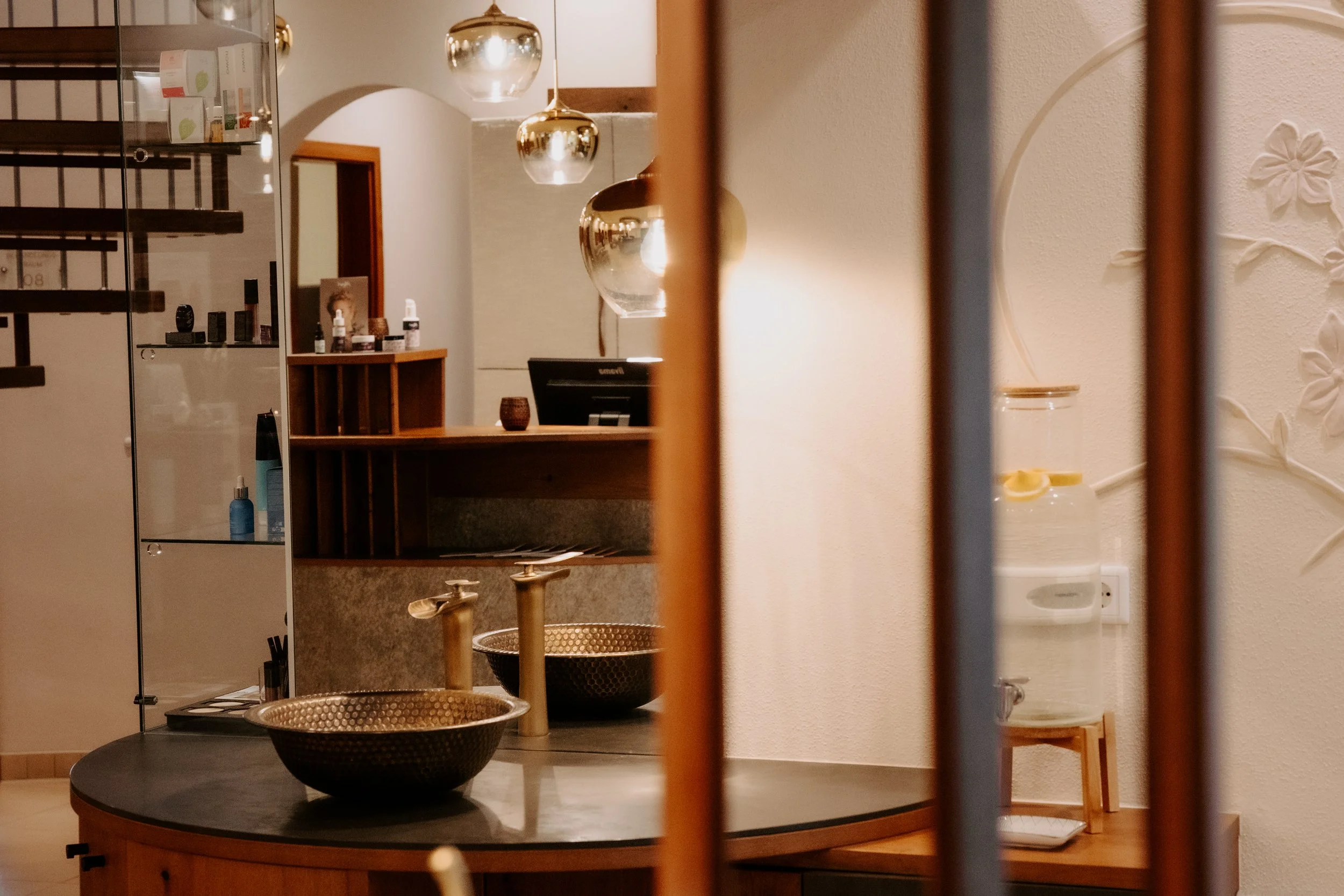 Inneneinrichtung eines Raumes mit Wasserfilter, Wasserkrug, dekorativen Deckenleuchten, Schreibtisch mit Computer und Spiegel. Deko-Elemente und Kosmetikartikel auf einem Regal.