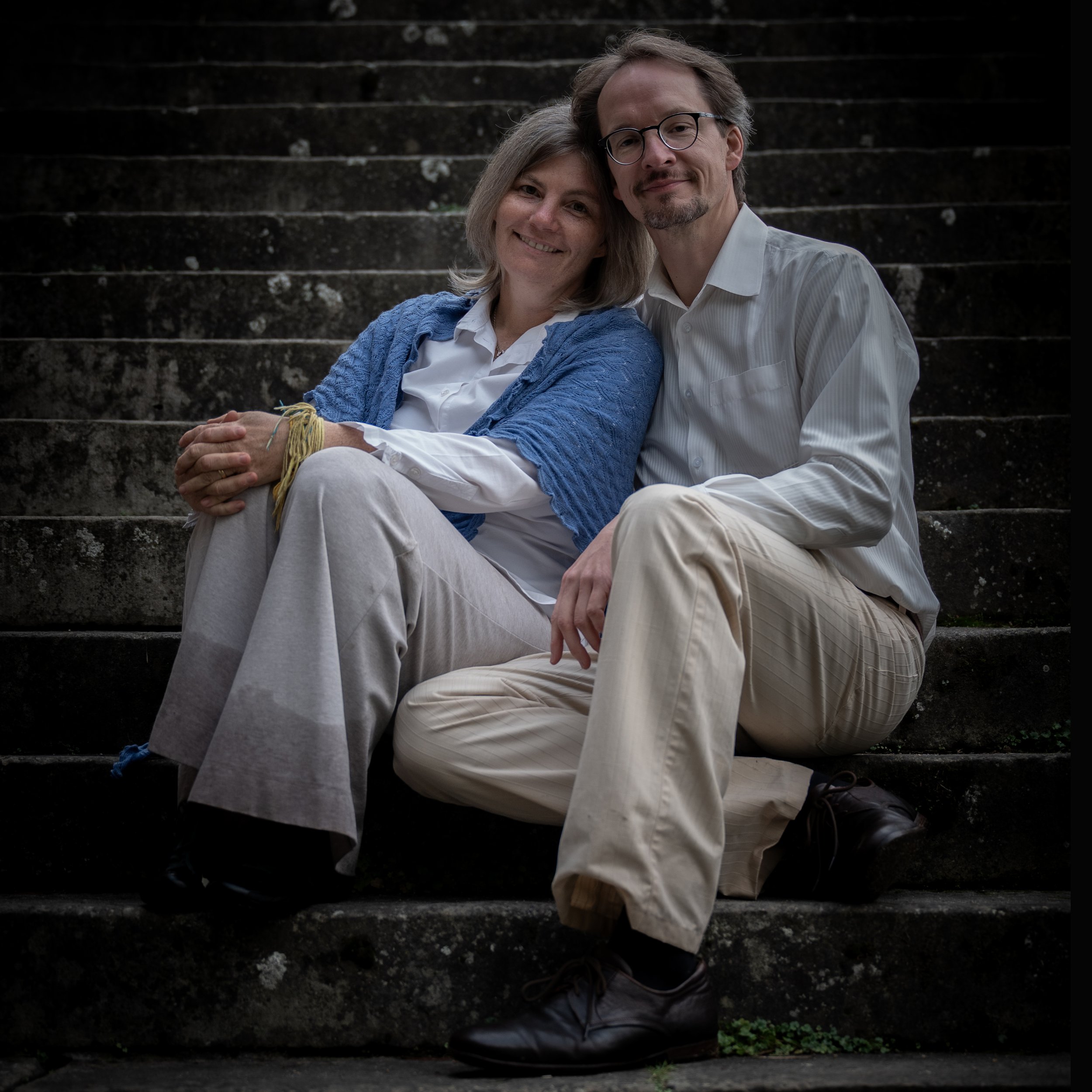 Ein älteres Paar sitzt auf einer Treppe draußen, lächelnd und umarmend.