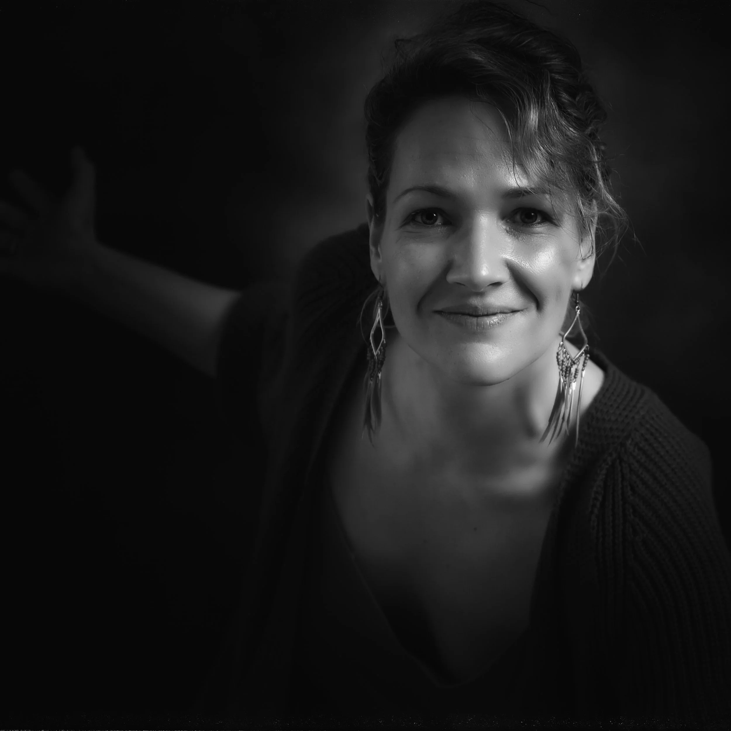 Schwarz-weiß-Fotografie eines lachenden jungen Mädchens mit kurzen, welligen Haaren und langen Ohrringen, das in die Kamera schaut.