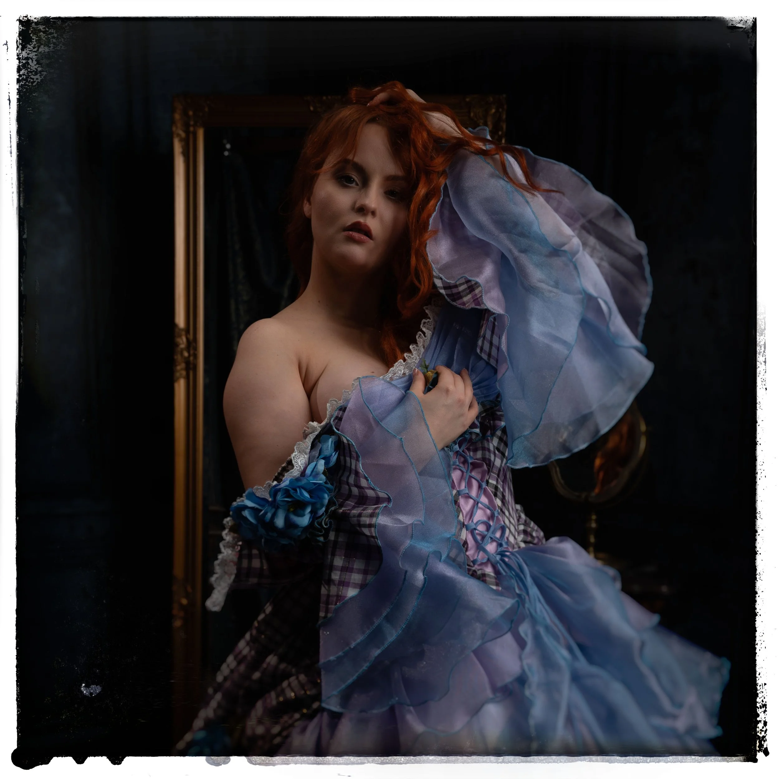 Porträt einer roten-haired Frau in einem viktorianischen Kleid mit blauen und lila Details vor einem dunklen Hintergrund, mit einem goldenen Rahmen im Hintergrund.