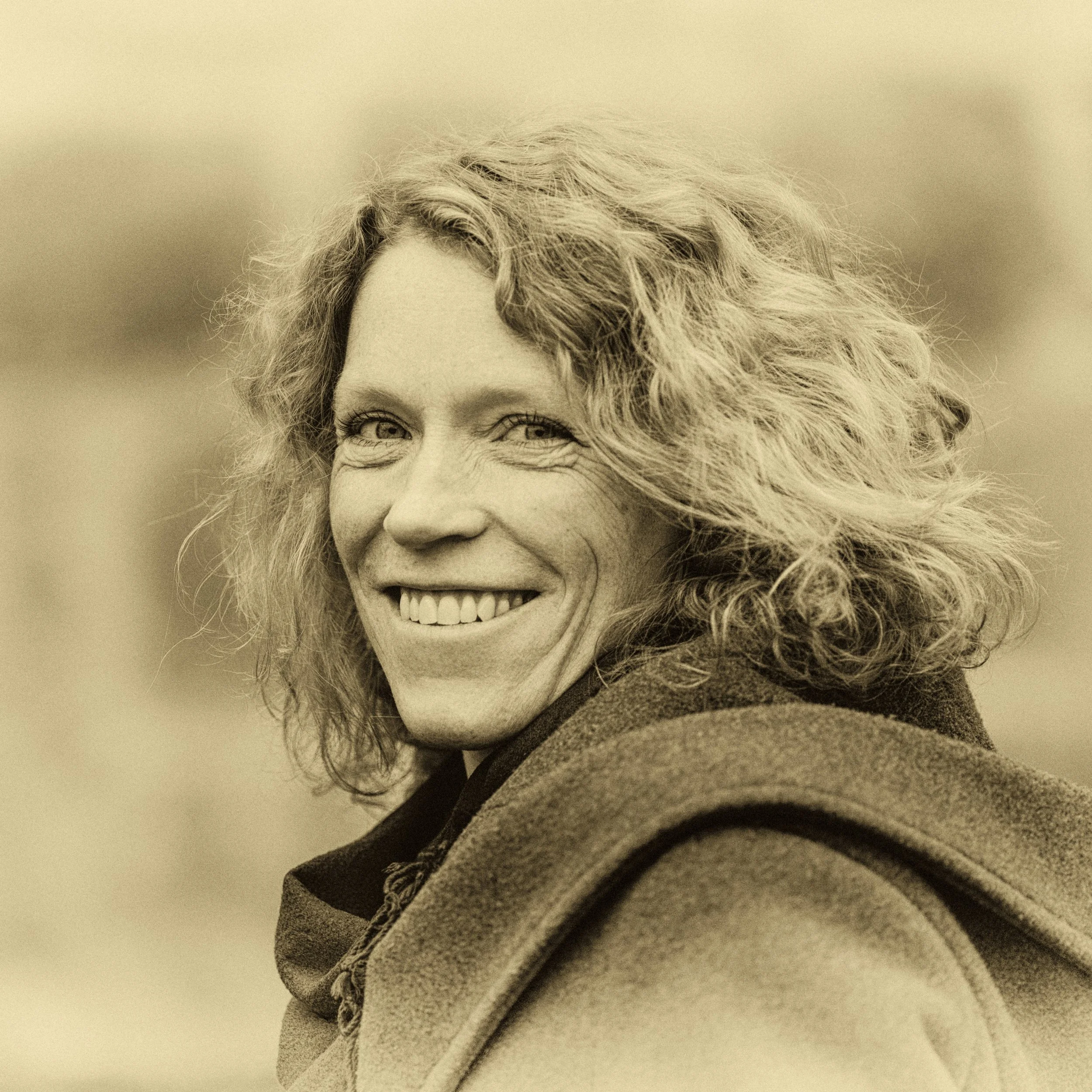 Nahaufnahme eines lachenden Mannes mit lockigem Haar in sepia Tönen.