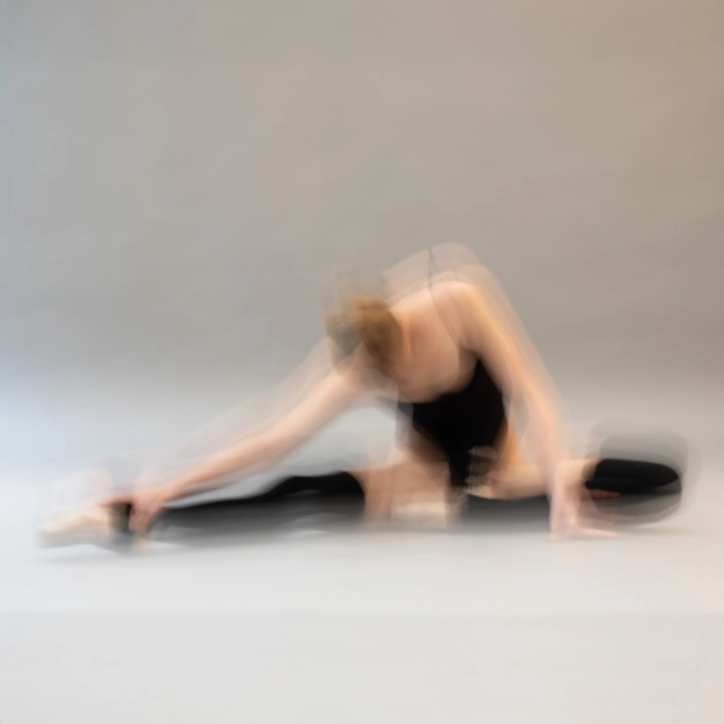Ein Tänzer in Bewegung, der sich auf dem Boden streckt, silhouttenartig gegen einen neutralen Hintergrund.