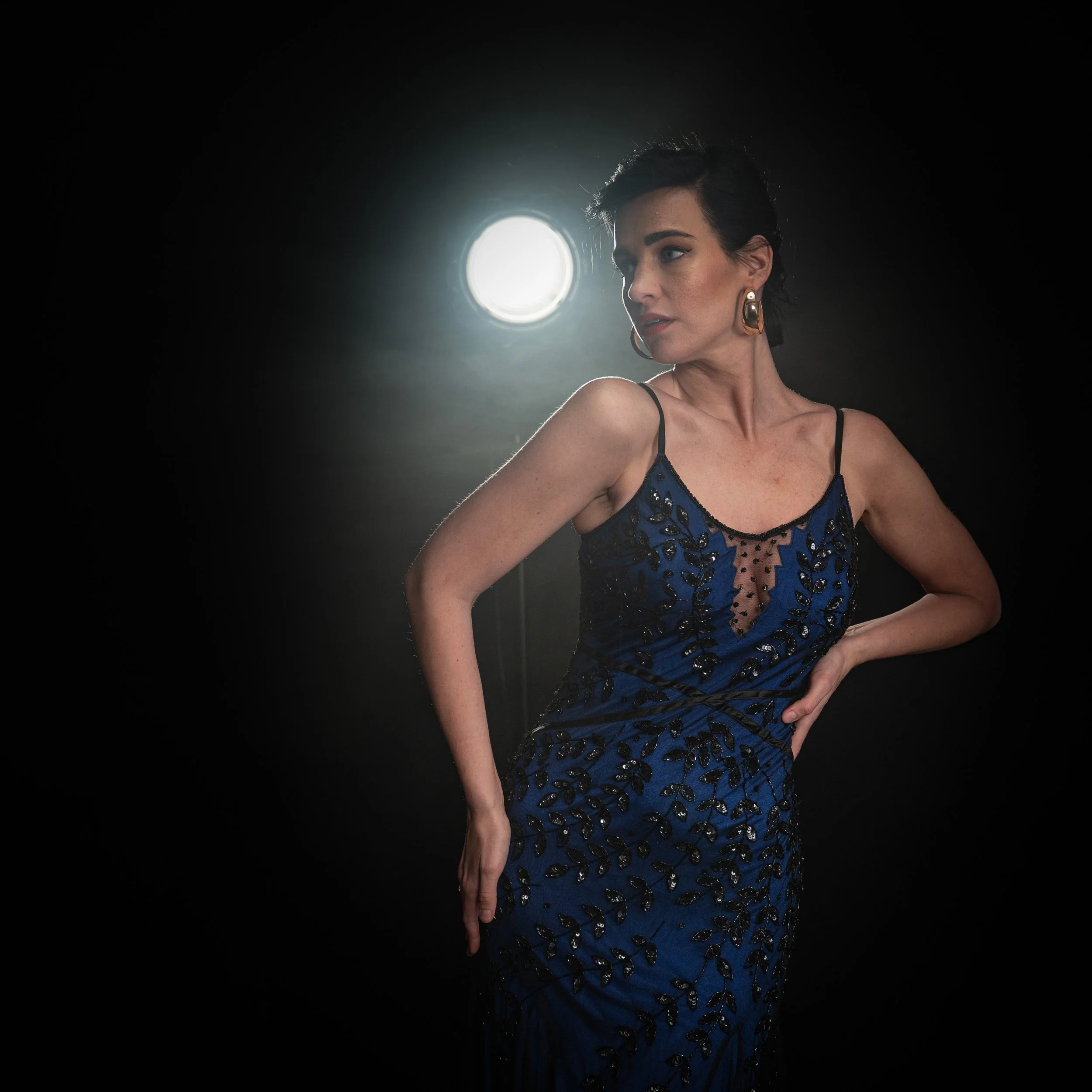 Frau in blauem Abendkleid vor dunklem Hintergrund mit Lichtquelle hinter ihr