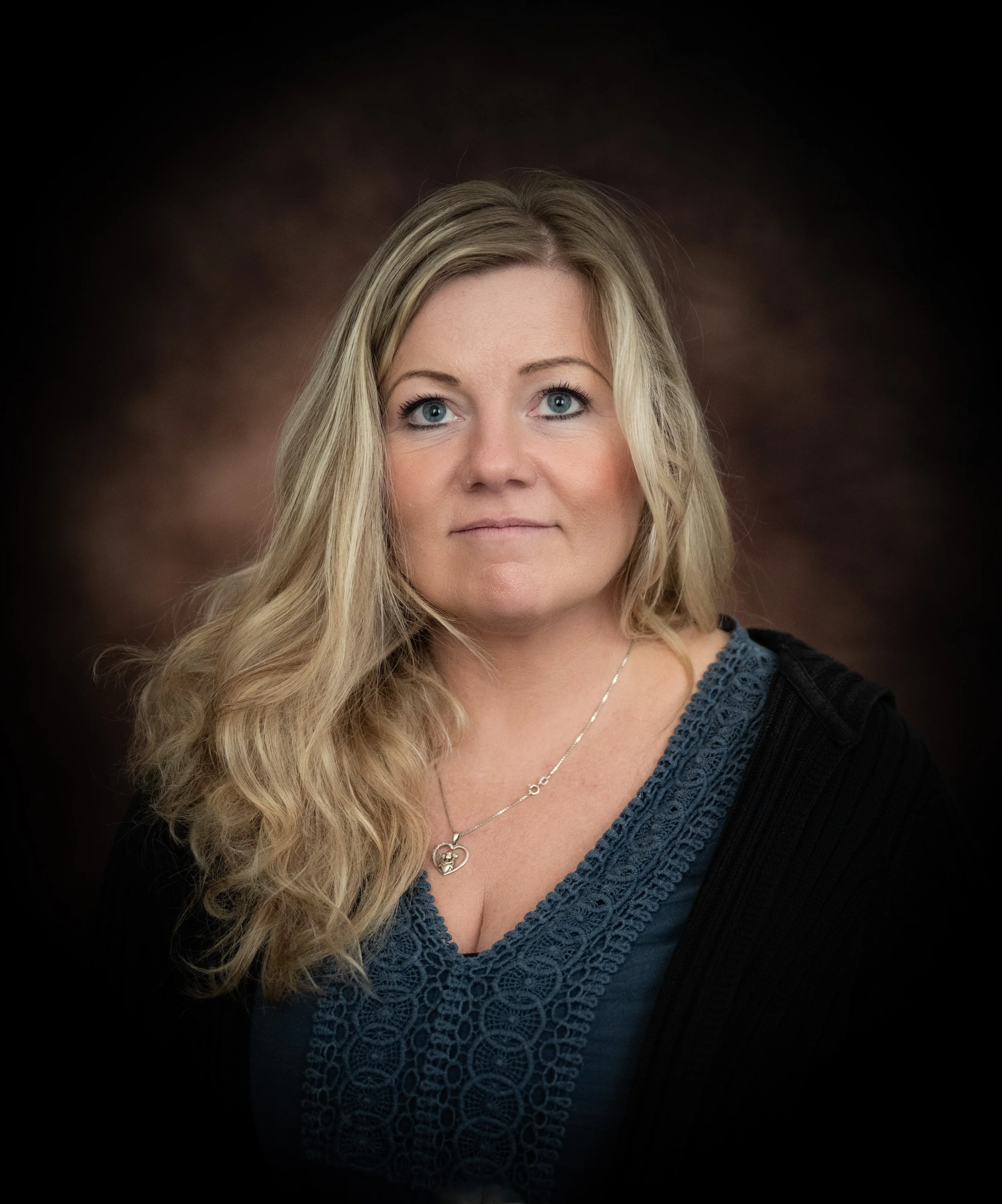 Porträt einer Frau mit langen, lockigen blonden Haaren vor dunklem Hintergrund.