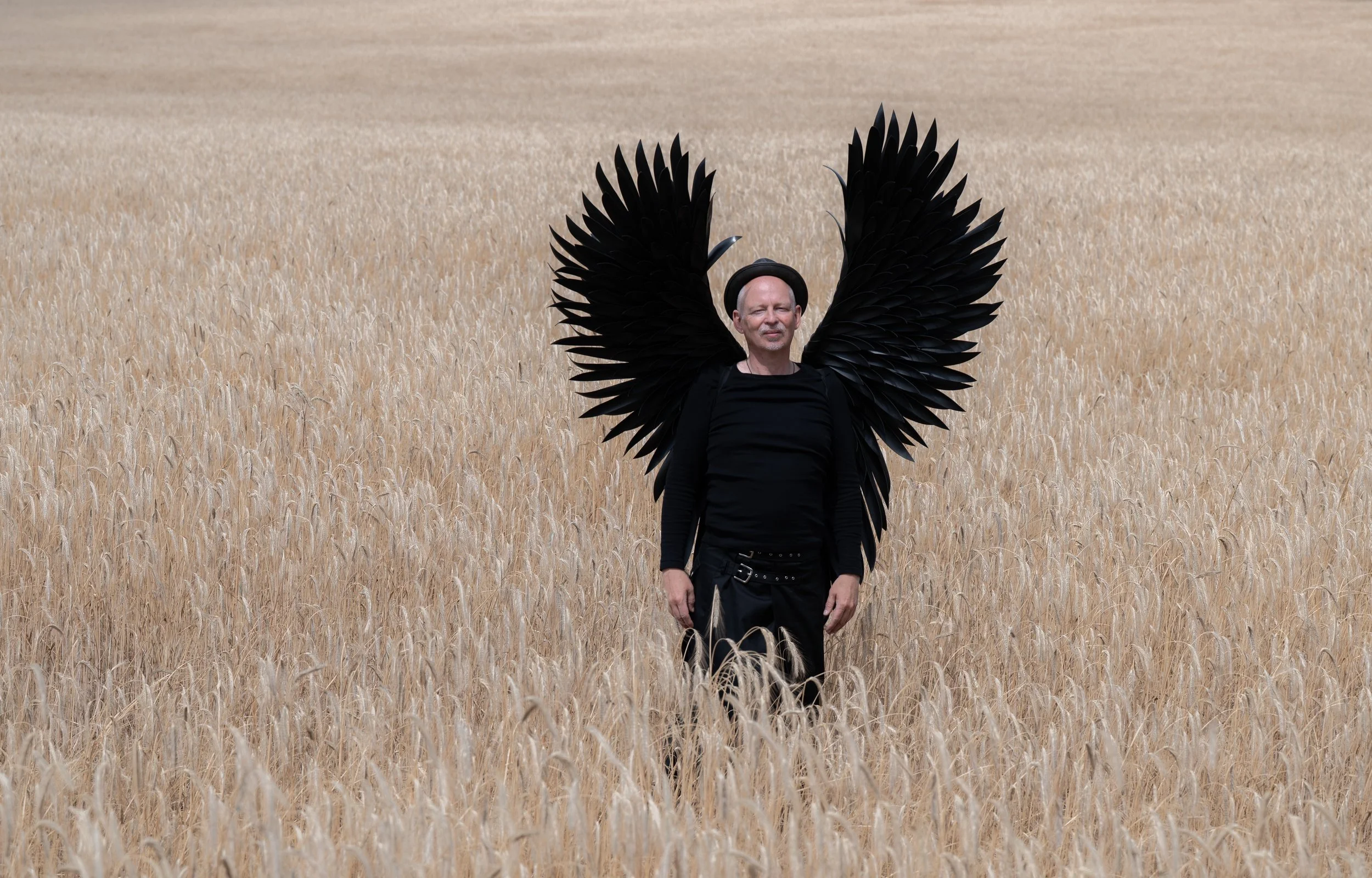 Mensch in schwarzen Flügeln steht in einem Weizenfeld.