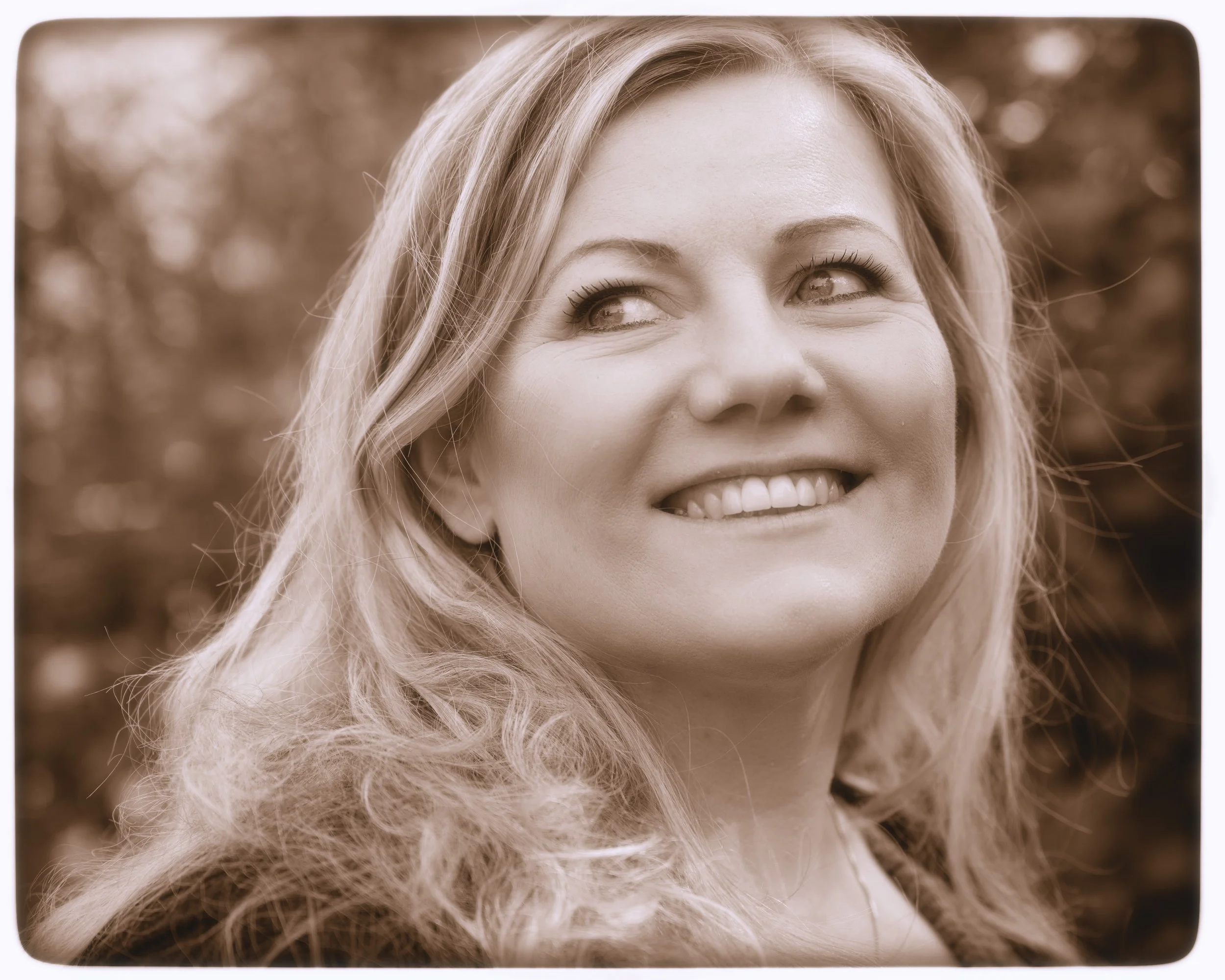 Ein lachendes Frauenporträt im Sepia-Ton mit lockigem, mittellangem Haar.