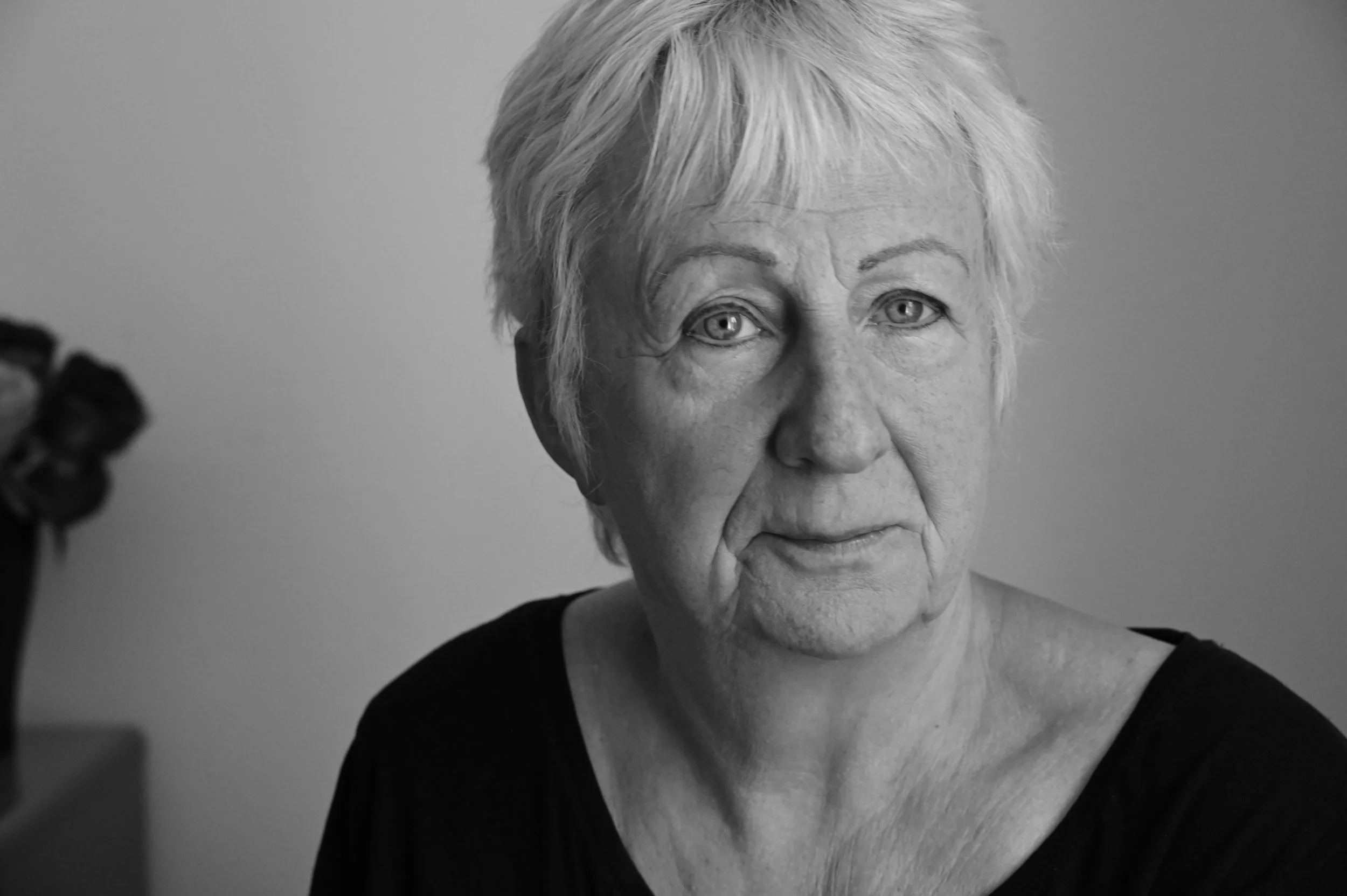Schwarz-weiß-Foto einer älteren älteren Frau mit kurzen, grauen Haaren, die in die Kamera schaut.
