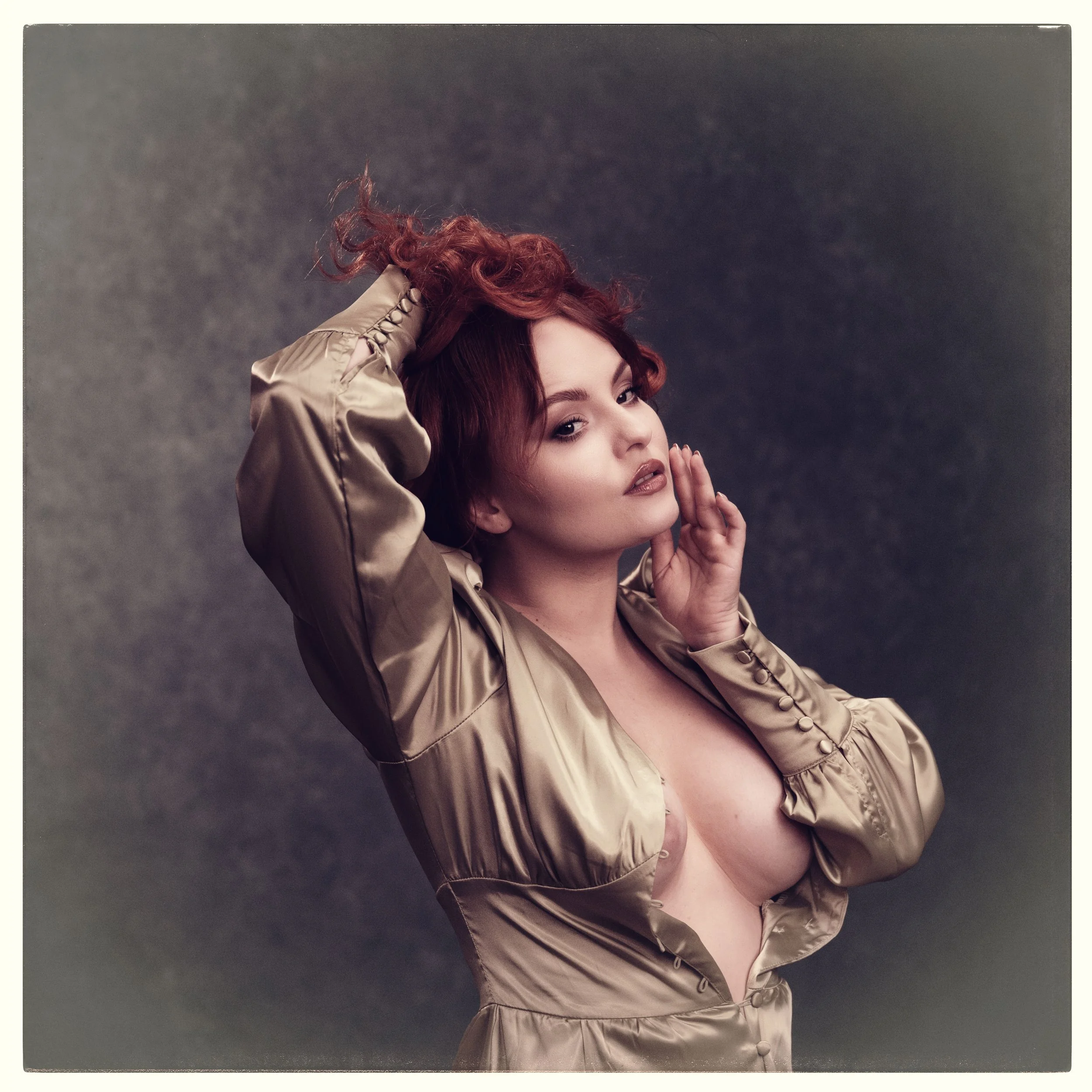 Eine Frau mit rotbraunen, lockigen Haaren, die einen vintage-look Satin-Button-down-Kleid trägt und sie an hat, posiert vor einem dunklen, neutralen Hintergrund.
