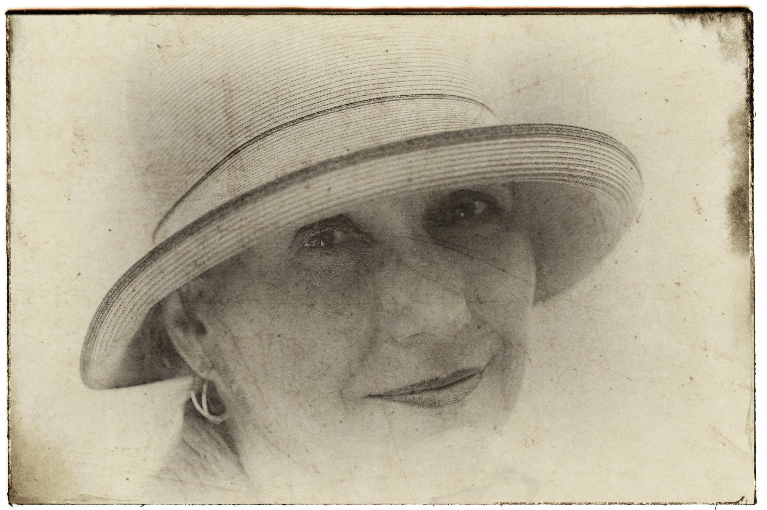 Schwarzweiß-Foto einer Frau mit Sonnenhut, die leicht lächelt.