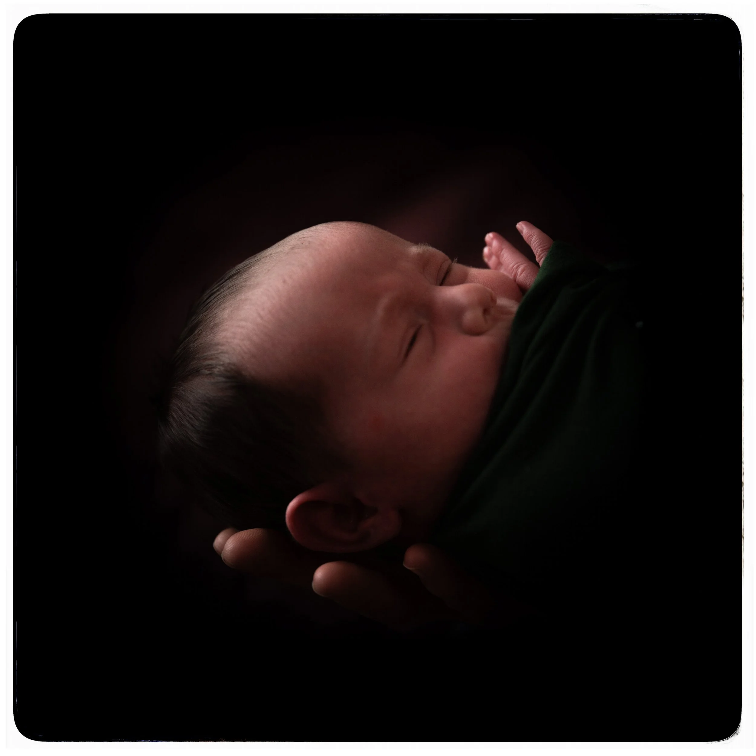 Nahaufnahme eines schlafenden Babys, das in einer Hand gehalten wird.