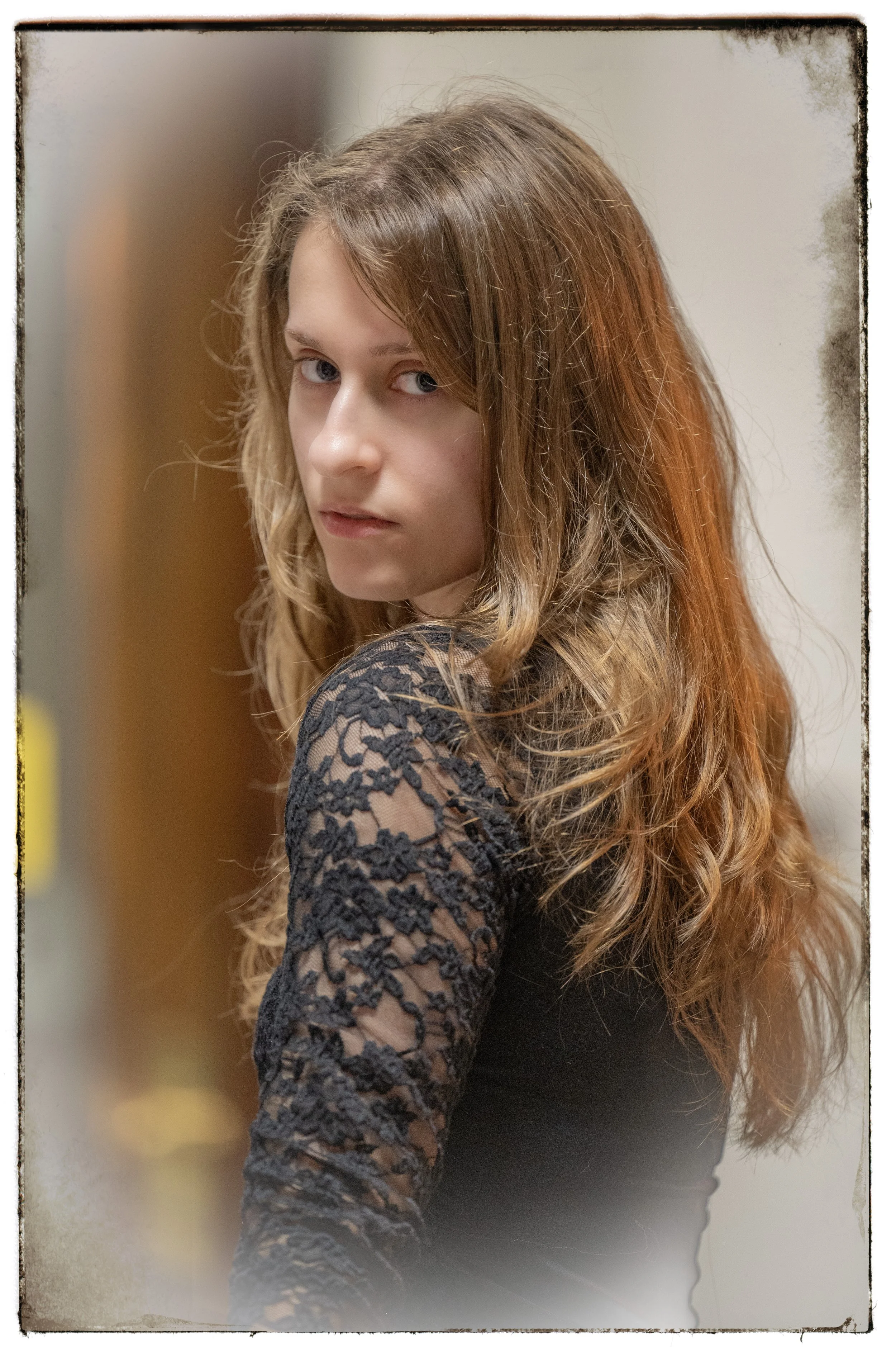 Junge Frau mit langen, gewellten braunen Haaren, die schwarzes Spitzenoberteil trägt, blickt seitlich, unscharfer Hintergrund