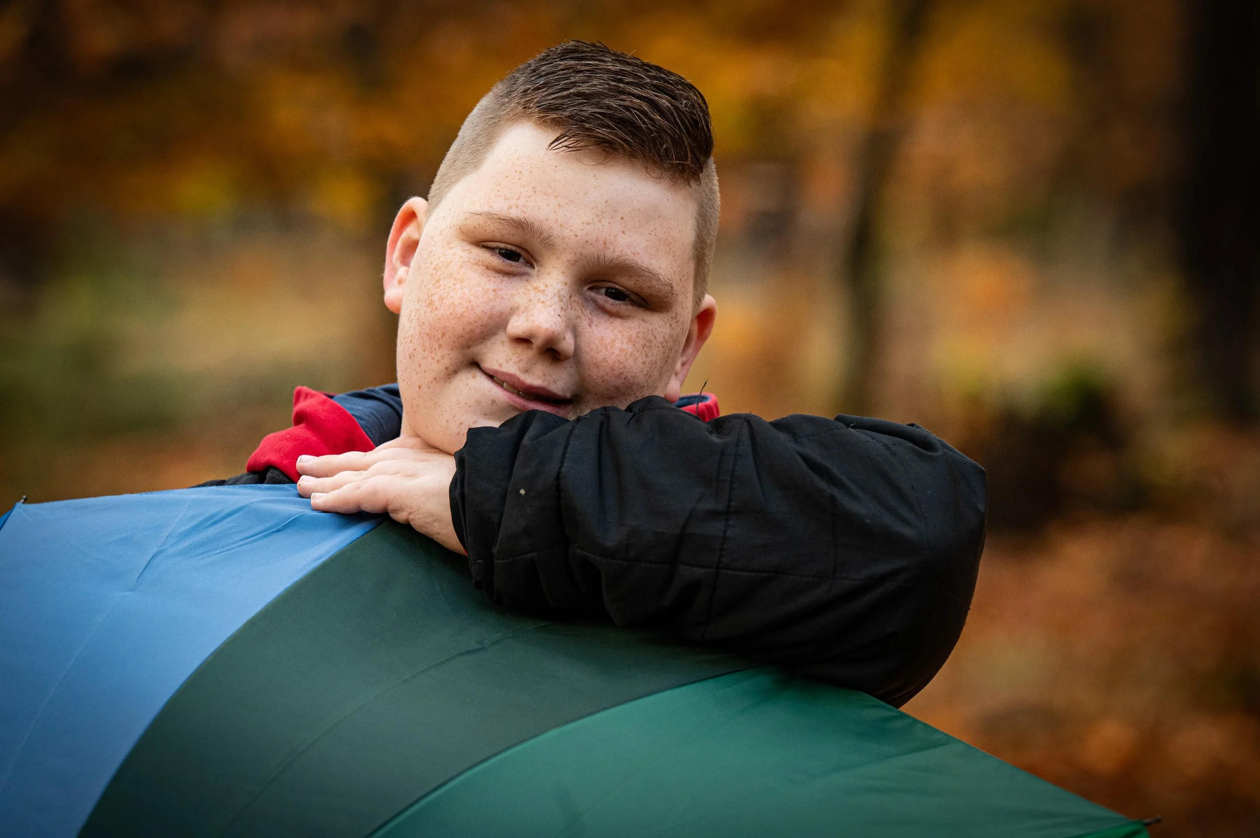 Junge mit kurzen braunen Haaren, Sommersprossen, entspannt auf einem bunten Tunnel in einem Herbstwald, lächelnd.