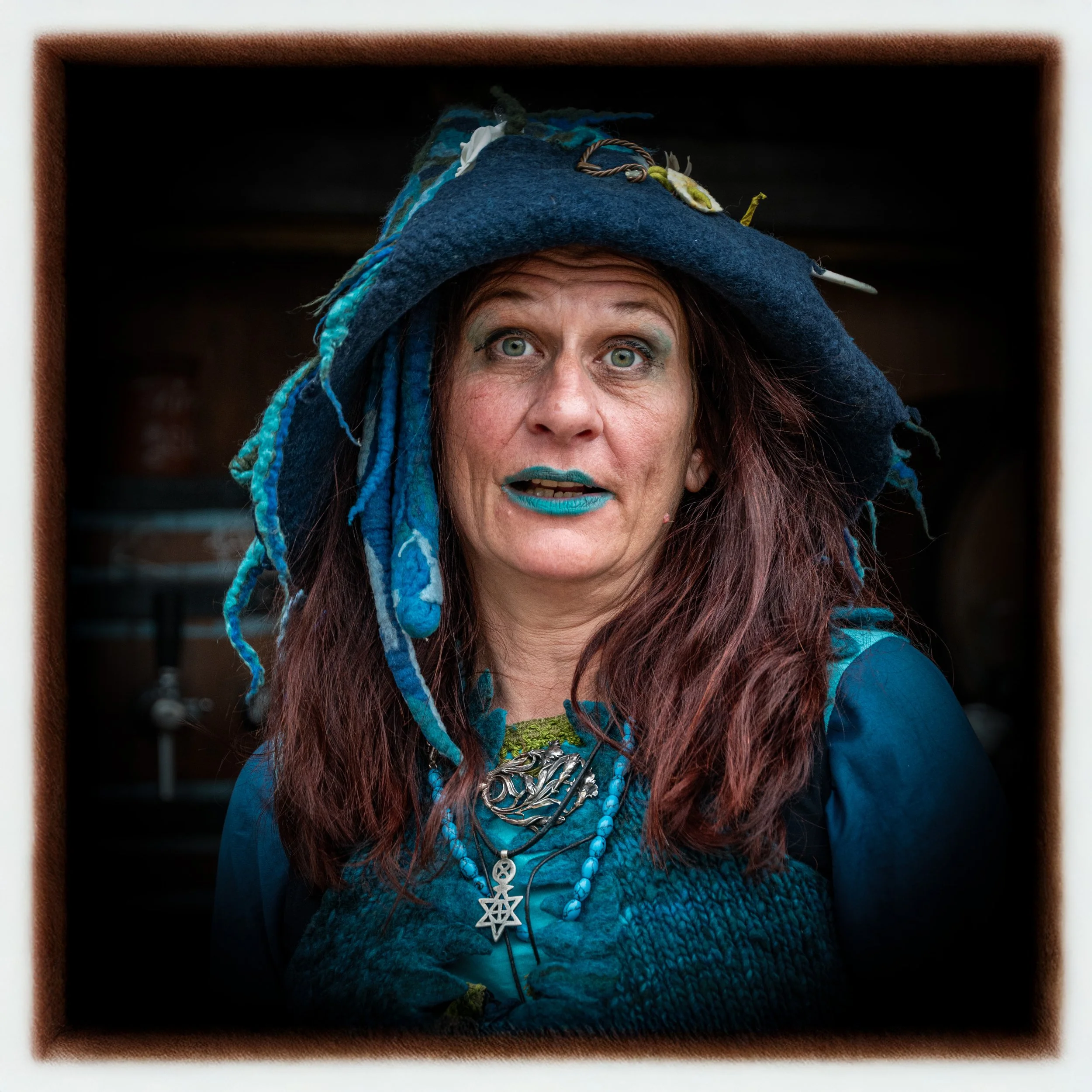 Frau im fantasievollen blauen Kostüm mit Hut, Dreadlocks und Schmuck.