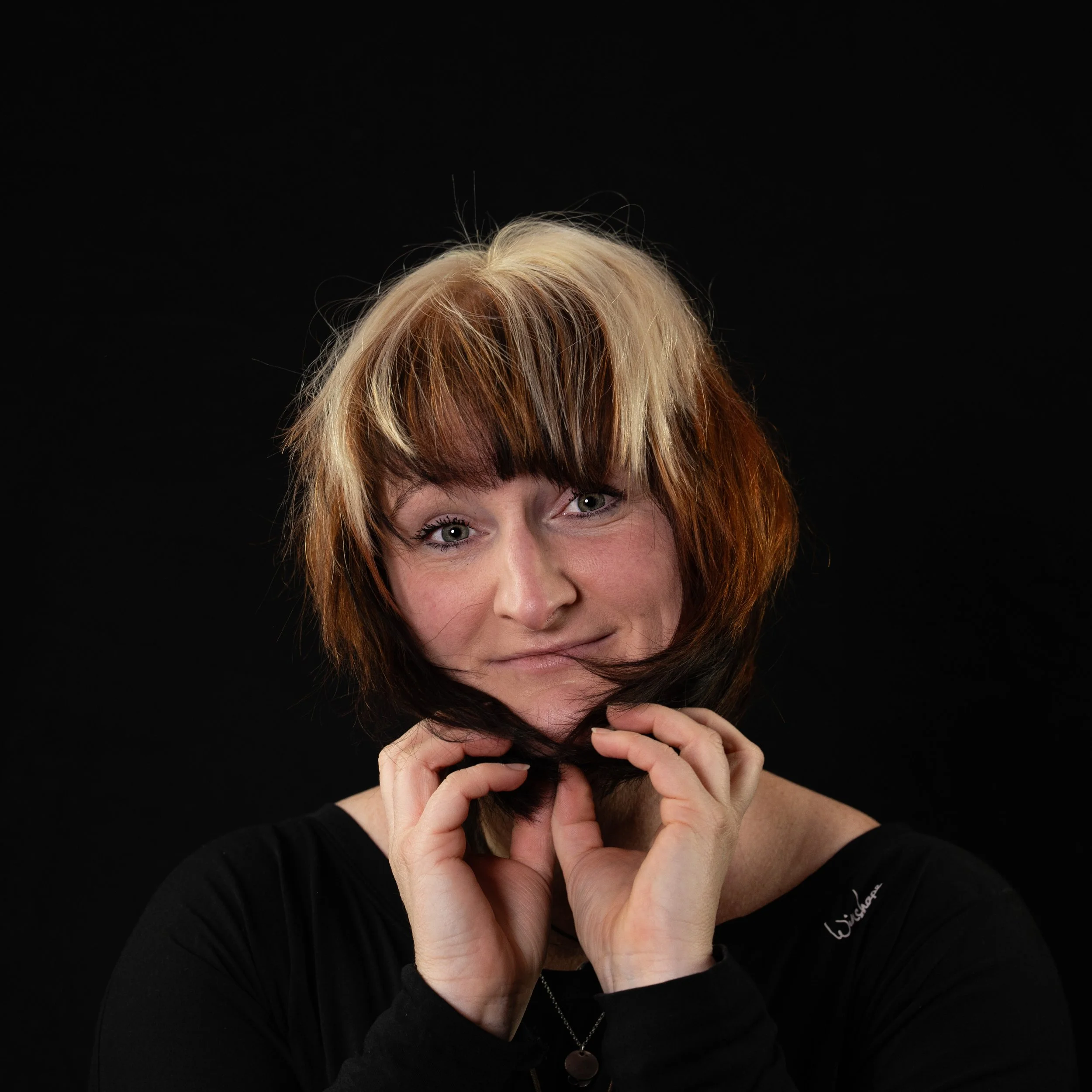 Porträt einer Frau mit kurzen, zweifarbigen Haaren, die einen schwarzen Hintergrund hat.