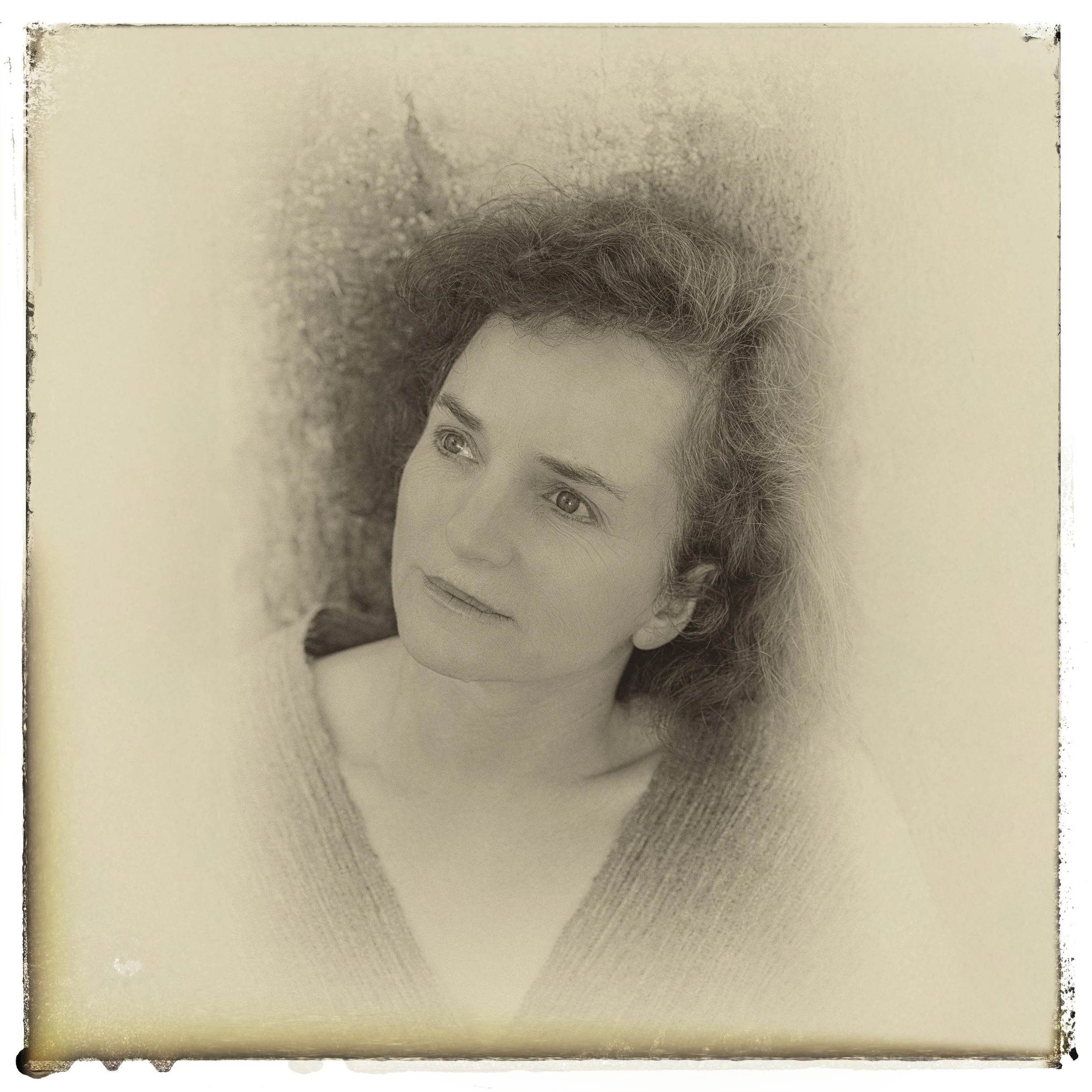 Porträt einer Frau mit lockigem Haar, die in die Ferne schaut, in sepiafarbenem Ton aufgenommen.