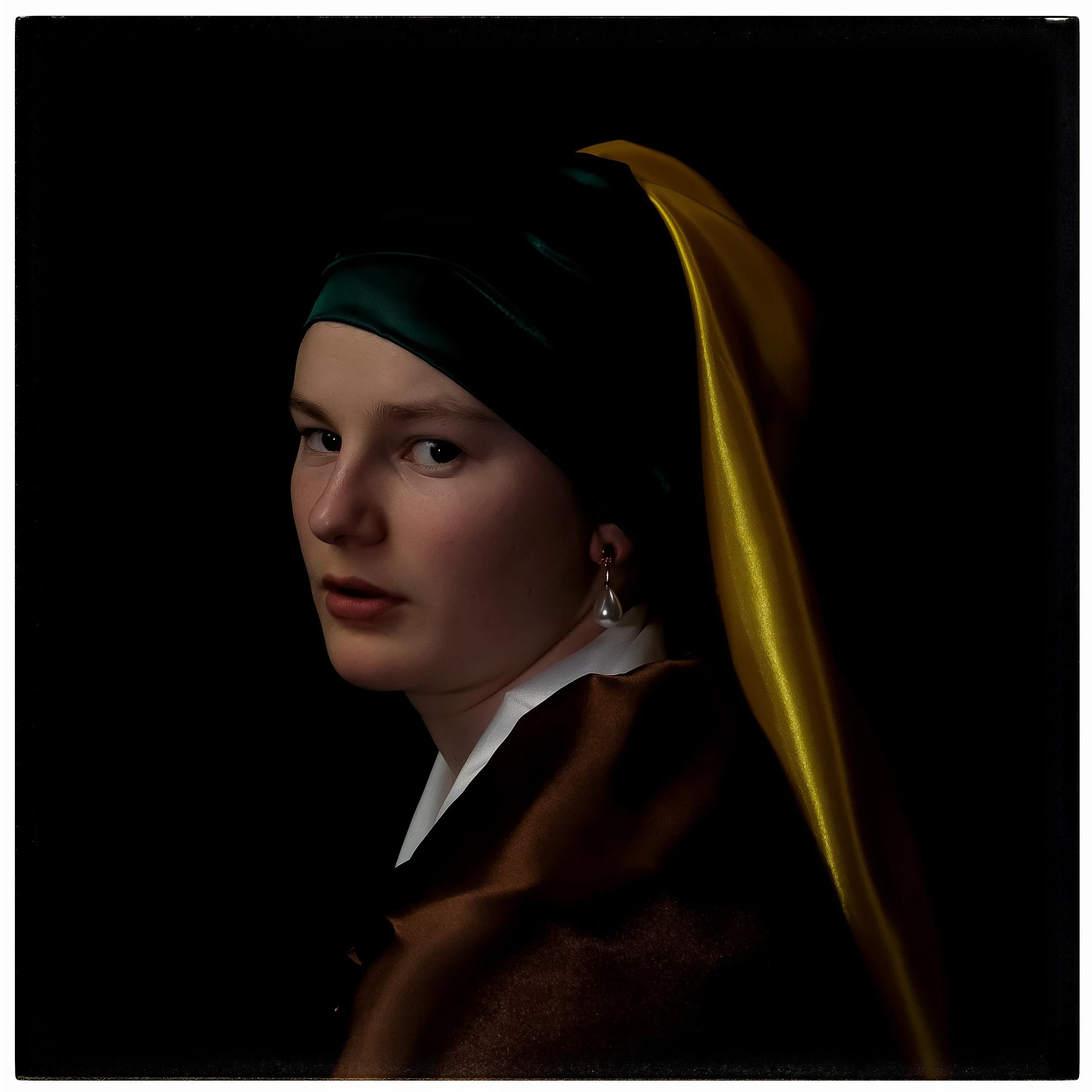 Porträt einer jungen Frau mit dunklem Hintergrund, trägt einen grünen und goldenen Schleier, weiße Bluse und einen braunen Mantel, trägt eine Perlenohrringe.