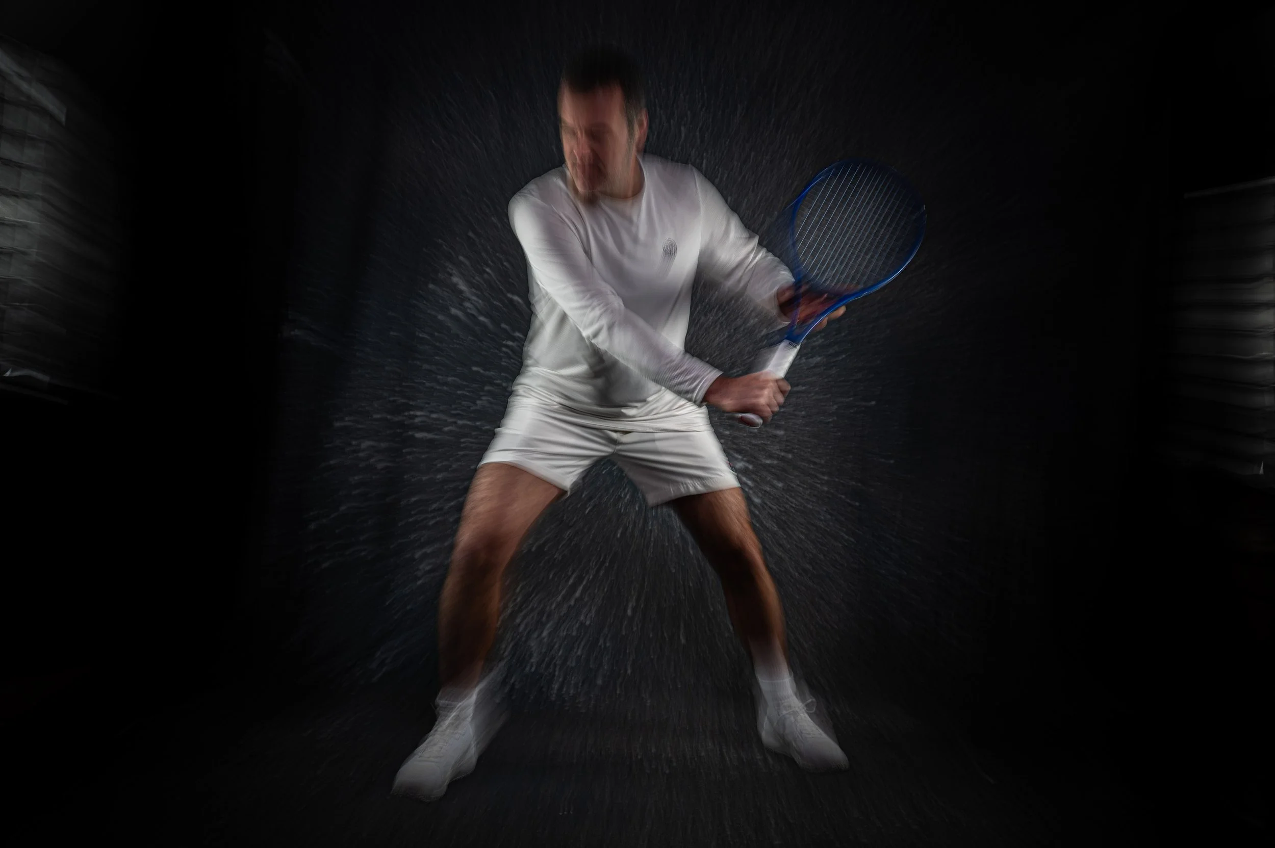 Mann in weißem Tennisoutfit schwingt mit Tennisracket, Wasser spritzt, dynamisch, dunkler Hintergrund.