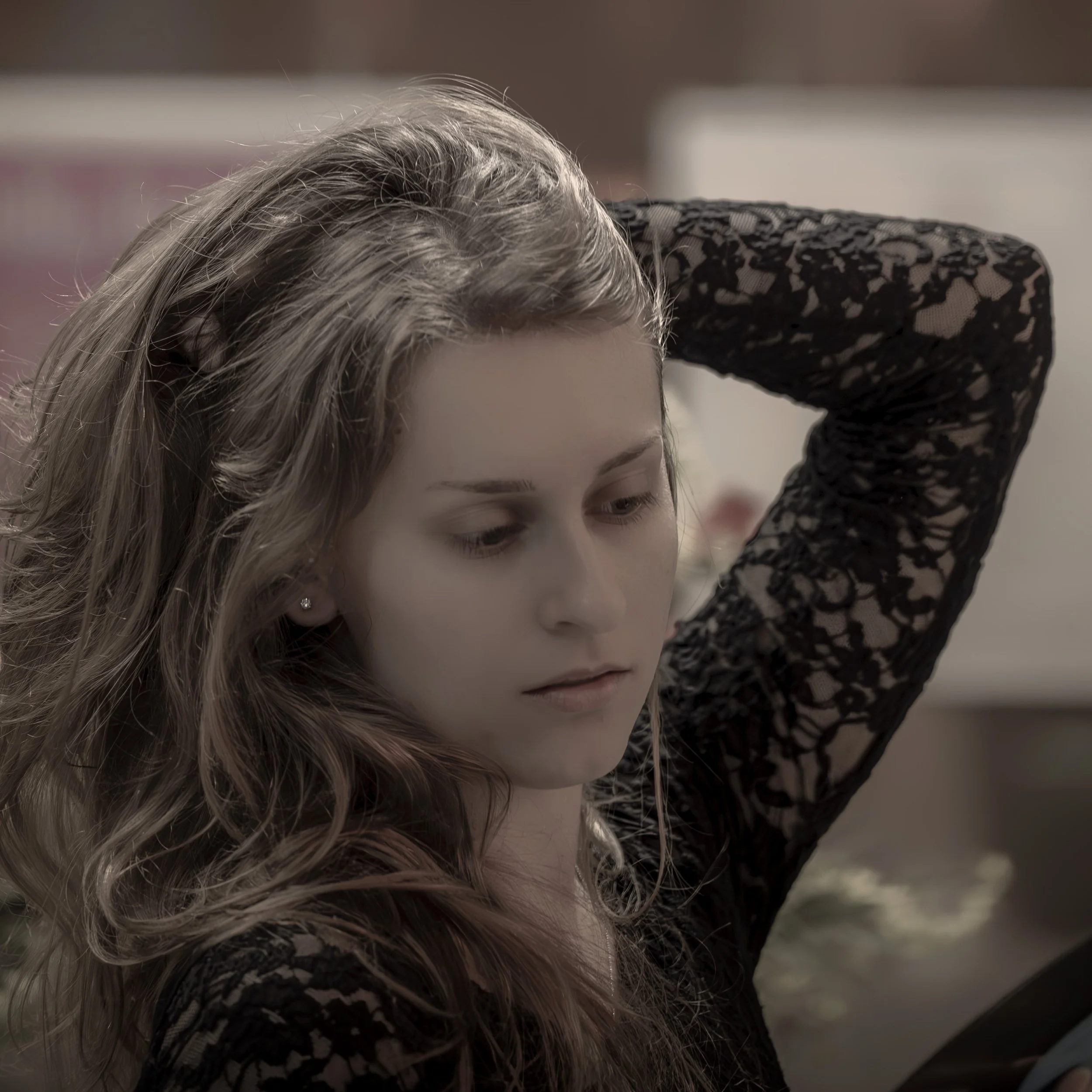 Junge Frau mit braunen, gewellten Haaren, die nach unten schaut, trägt ein schwarzes Spitzenoberteil und hat ein Ohrring im Ohr.