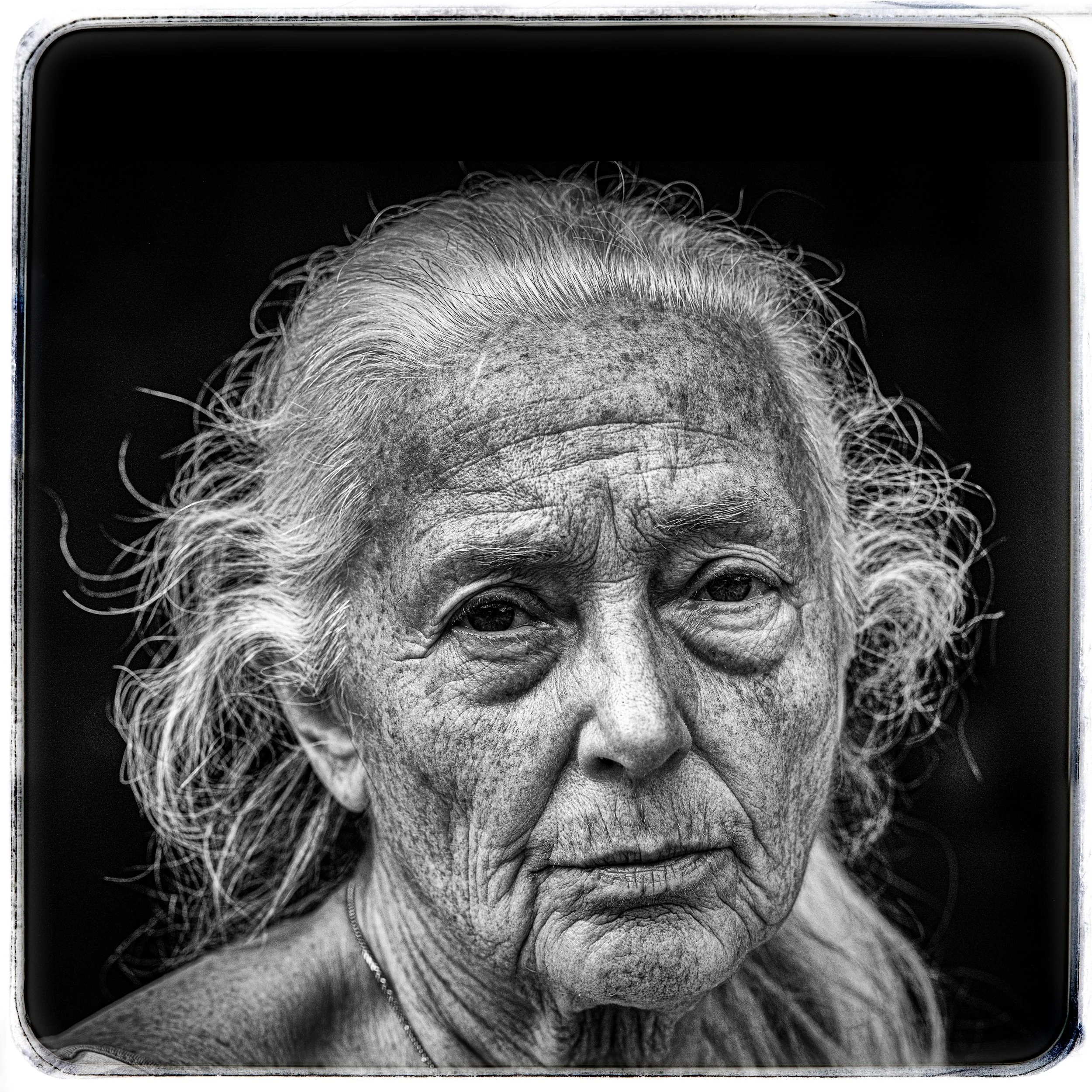 Schwarz-weiße Nahaufnahme eines älteren Frauenporträts mit silbergrauem, lockigem Haar und sichtbaren Gesichtsfalten.