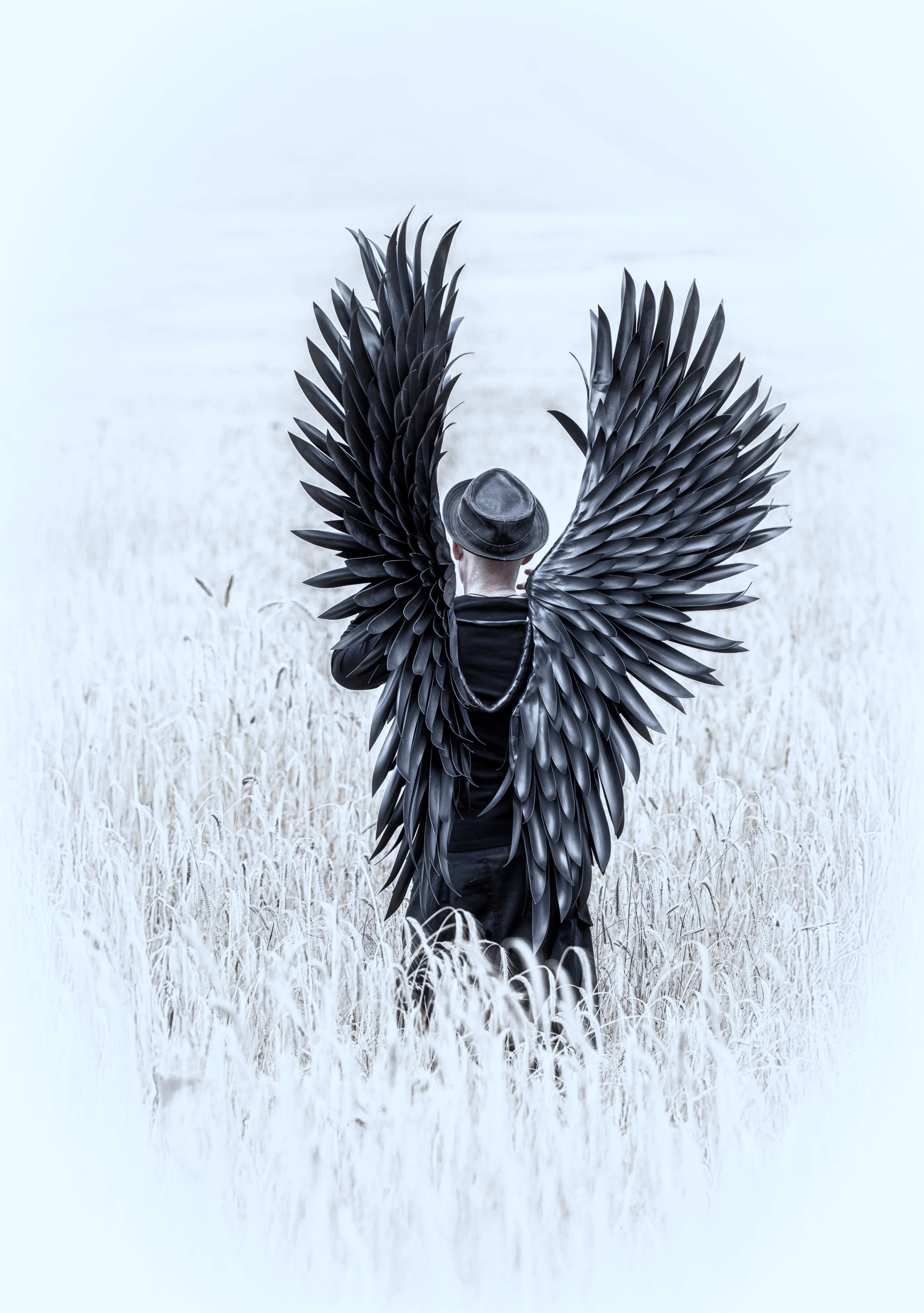 Person mit schwarzen Flügeln in einem weißen Feld, trägt einen Hut, Rückenansicht.