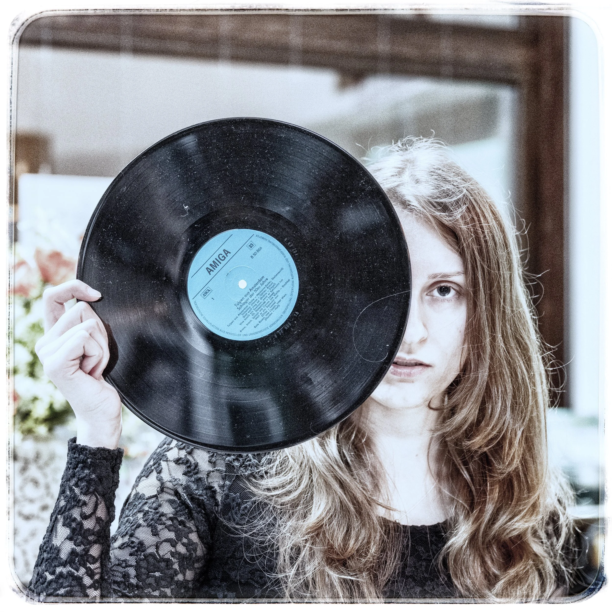 Junge Frau mit langem, lockigem Haar hält eine schwarze Vinyl-Schallplatte vor ihr Gesicht, sodass nur ihr Auge und Teil des Gesichts sichtbar sind.