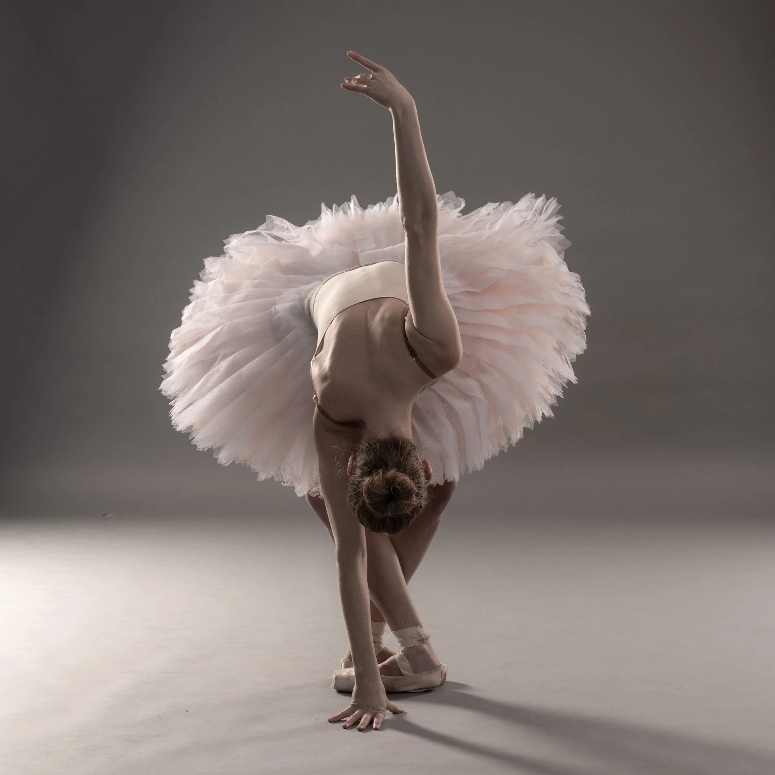 Tänzerin in Ballettkleidung macht einen Ballettschwung auf grauem Hintergrund.