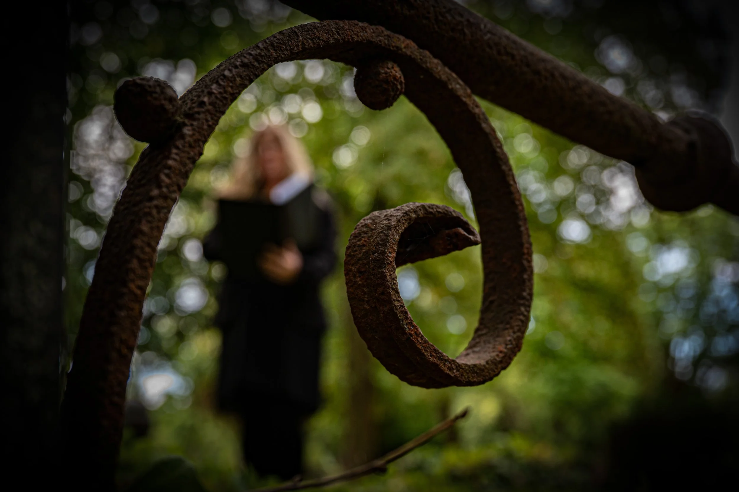 Rostige Eisenkette im Vordergrund, unscharfe Frau mit Laptop im Hintergrund in einem grünen Park.