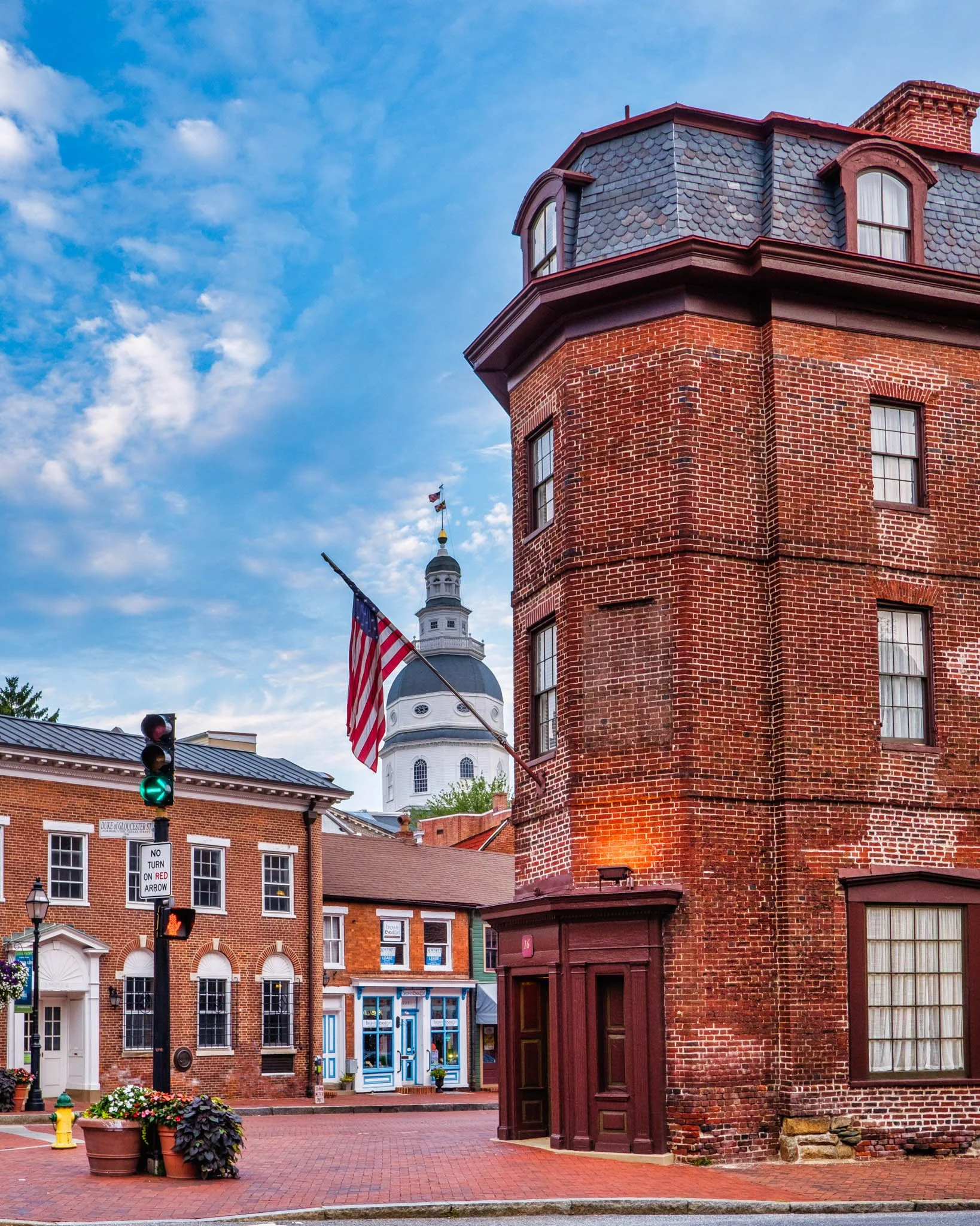 Street scene with brick buildings, American flag, traffic light, and a white domed building with a statue on top.