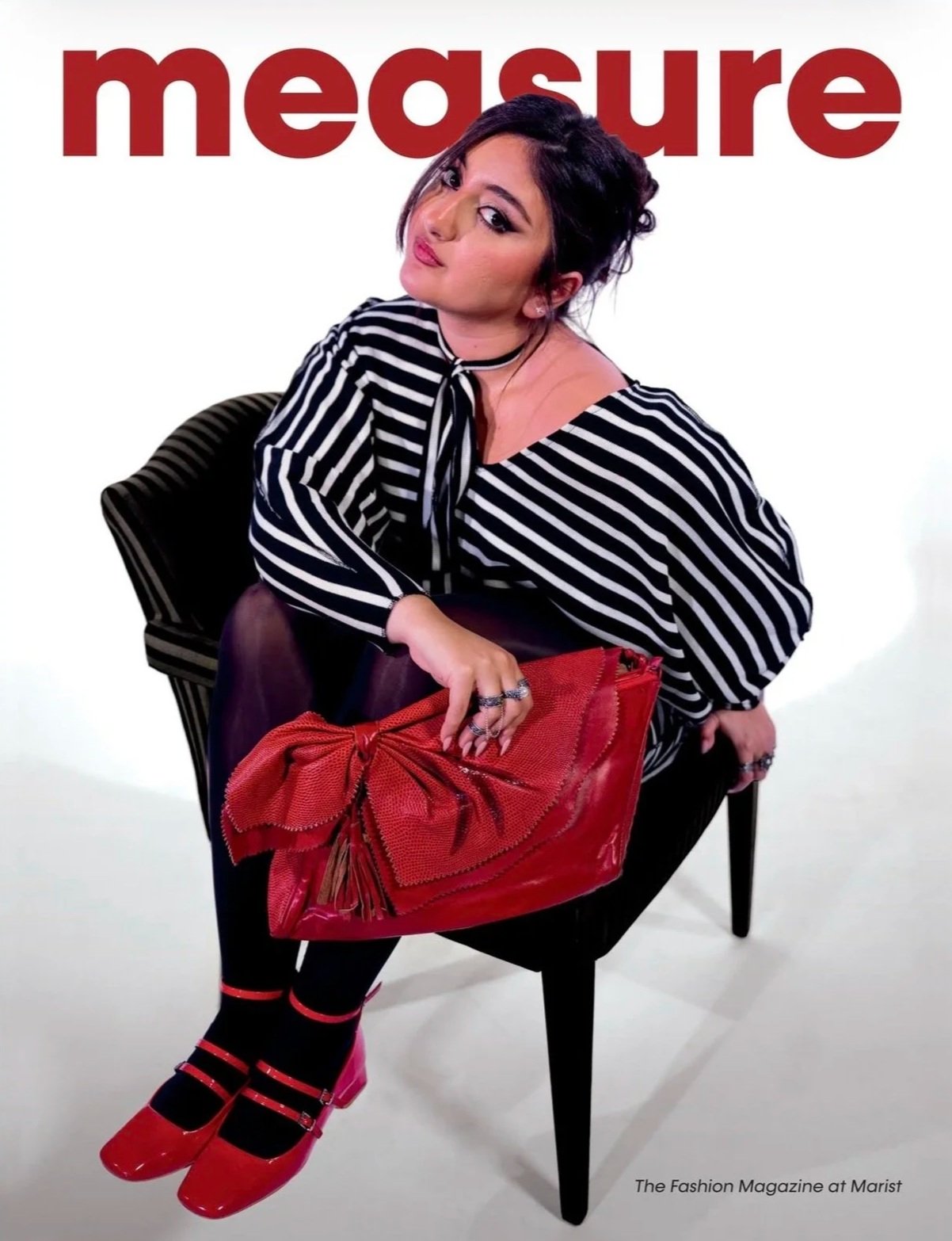 A woman sitting on a black chair with a white background and the word 'measure' in large red letters behind her. She is wearing a black and white striped blouse, red shoes, and holding a red handbag with a bow. The phrase "The Fashion Magazine at Marist" appears in the bottom right corner.