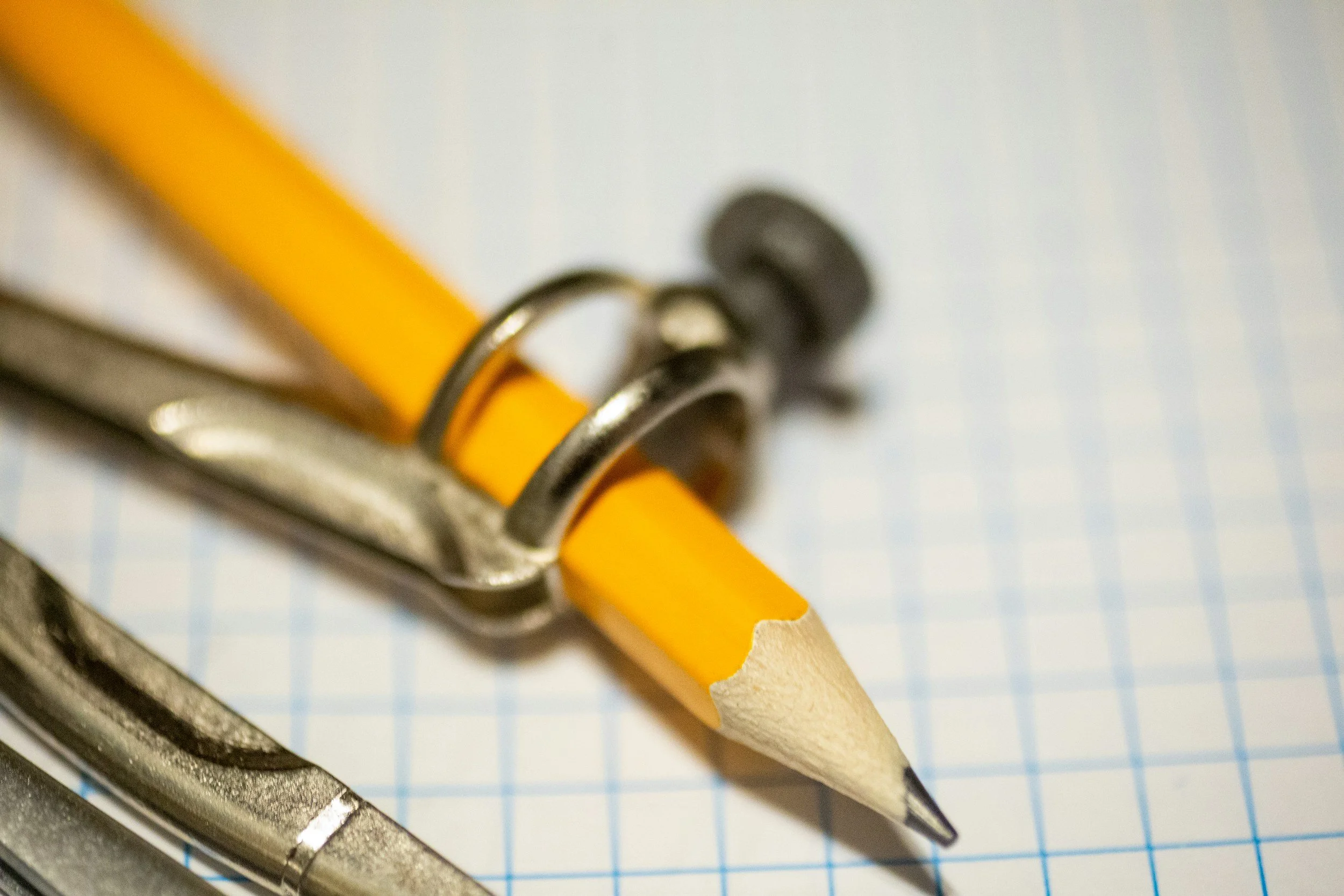 A yellow pencil with a metal clip resting on a sheet of graph paper, with a metal compass nearby, just one tool of Property Inspectors.